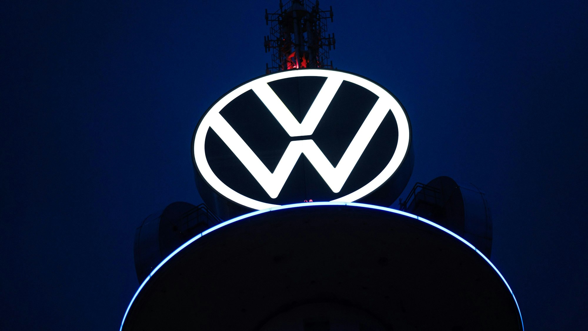 Das Volkswagen Logo leuchtet auf dem VW-Tower vor dunklem Himmel.
