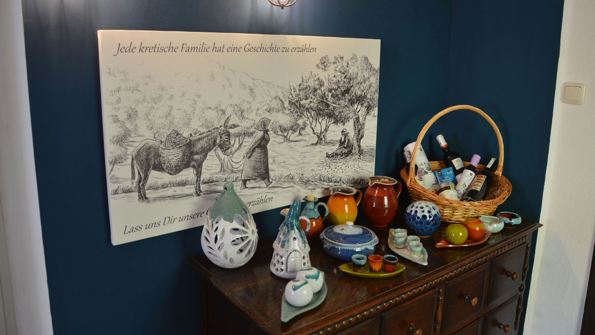 Vor einem Gemälde an der Wand steht Keramik aus Kreta auf einem Schränkchen.