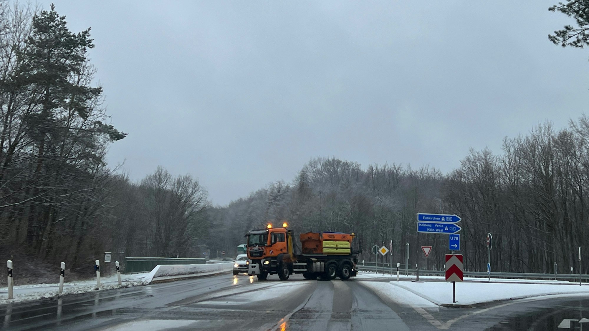 Das Foto zeigt ein orange-farbiges Streufahrzeug, das den Bereich einer Autobahnauffahrt streut und räumt.