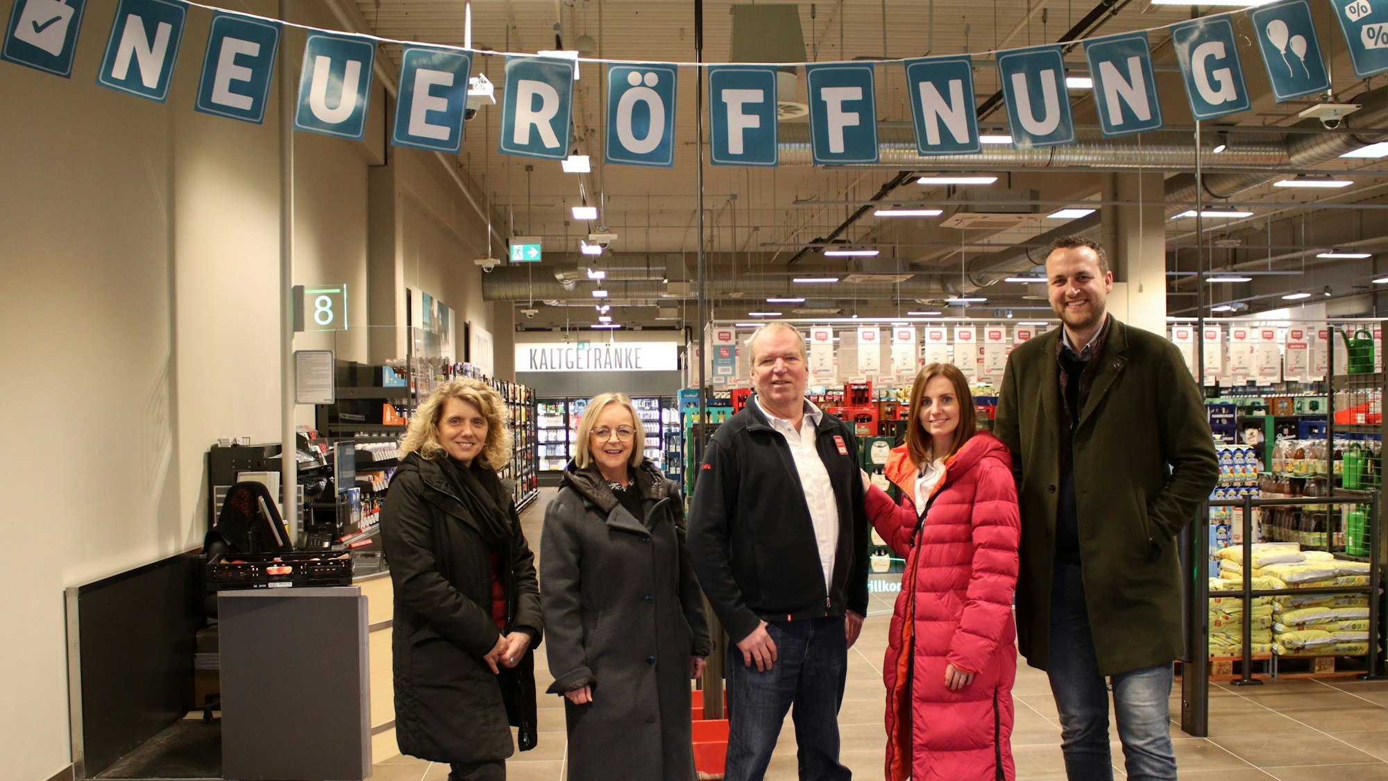 Carmen Haltenhof (v.l.), Sabine Preiser-Marian, Achim Horbach, Rebecca Thelen und Sebastian Strzelczyk posieren im Eingangsbereich des Rewe-Centers unter einem Neueröffnungsschild.