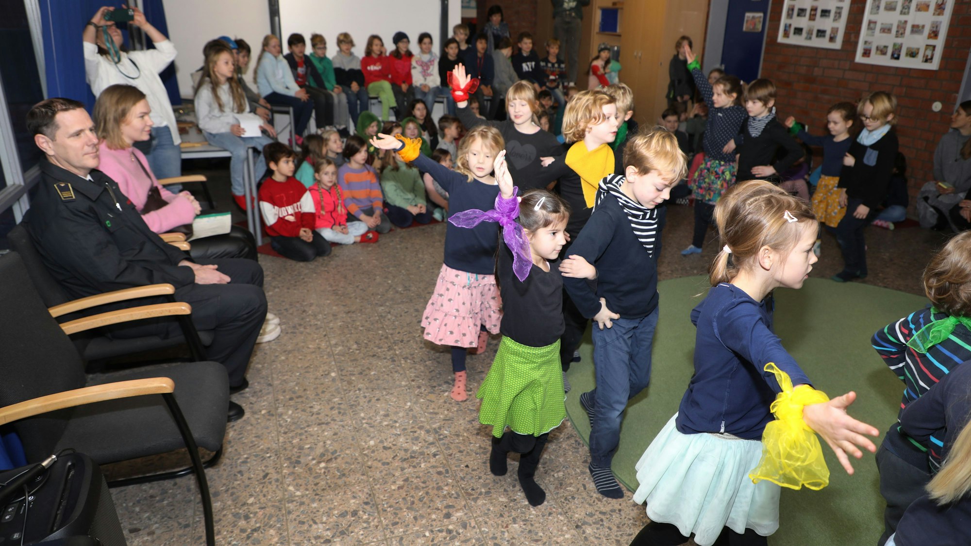 Kinder tanzen, andere schauen wie drei Erwachsene am Rand zu.