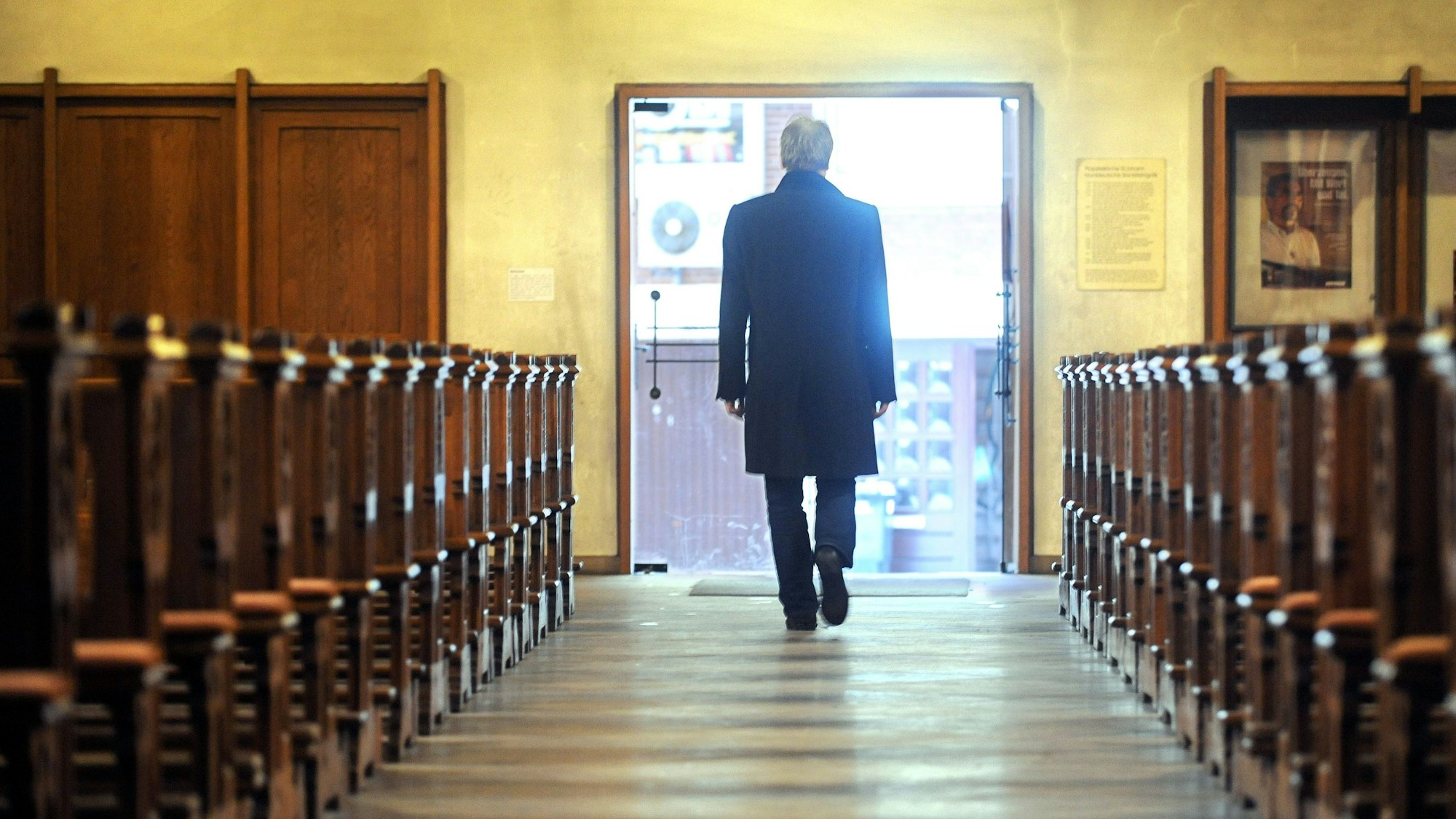 Zu sehen ist ein Mann, der eine Kirche durch den Mittelgang verlässt und Richtung geöffneter Ausgangstür geht.