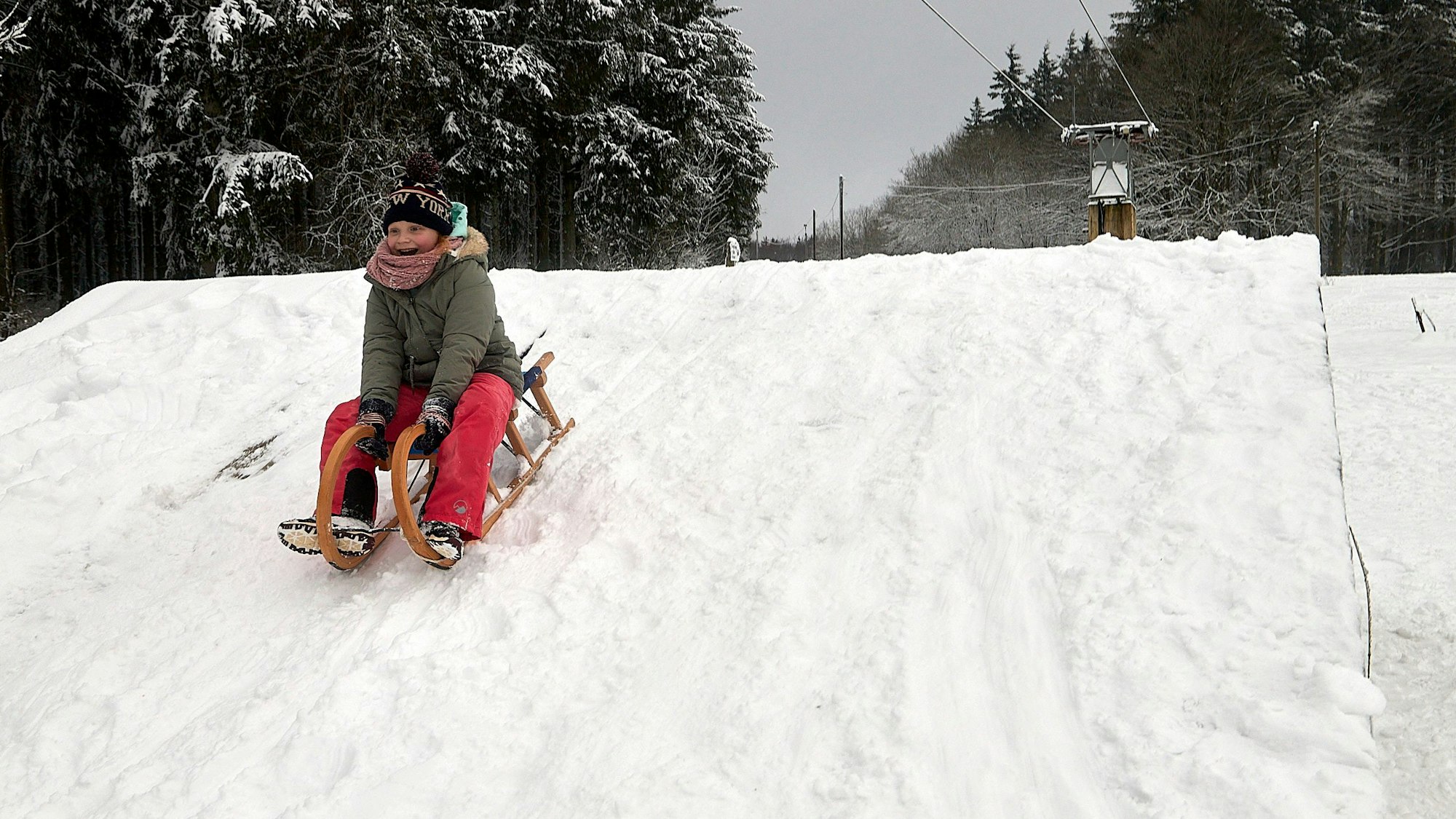 Ein Kind sitzt auf einem Schlitten und fährt einen Hügel runter.