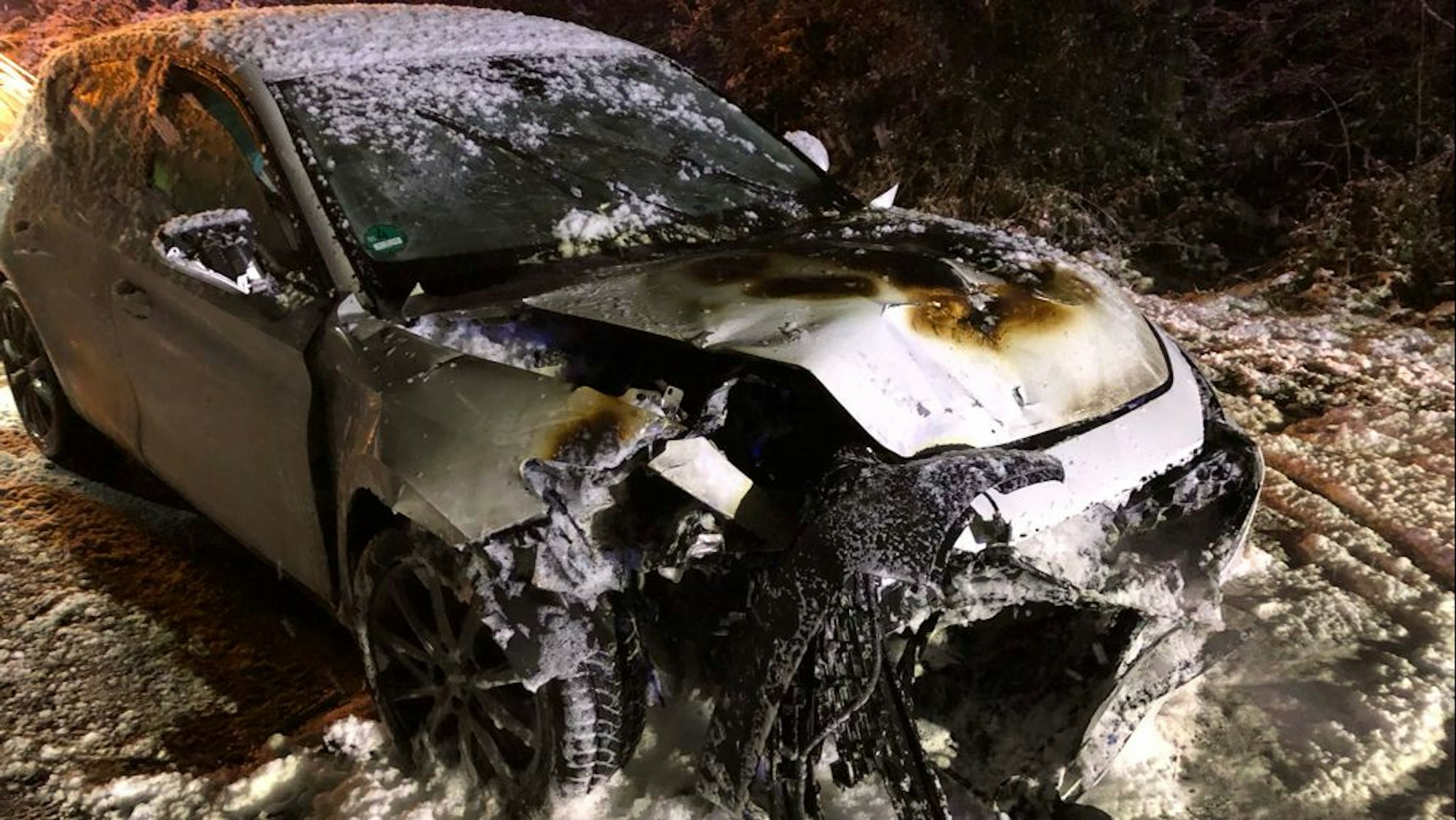 Ein ausgebranntes Fahrzeug steht auf einer winterlichen Straße.