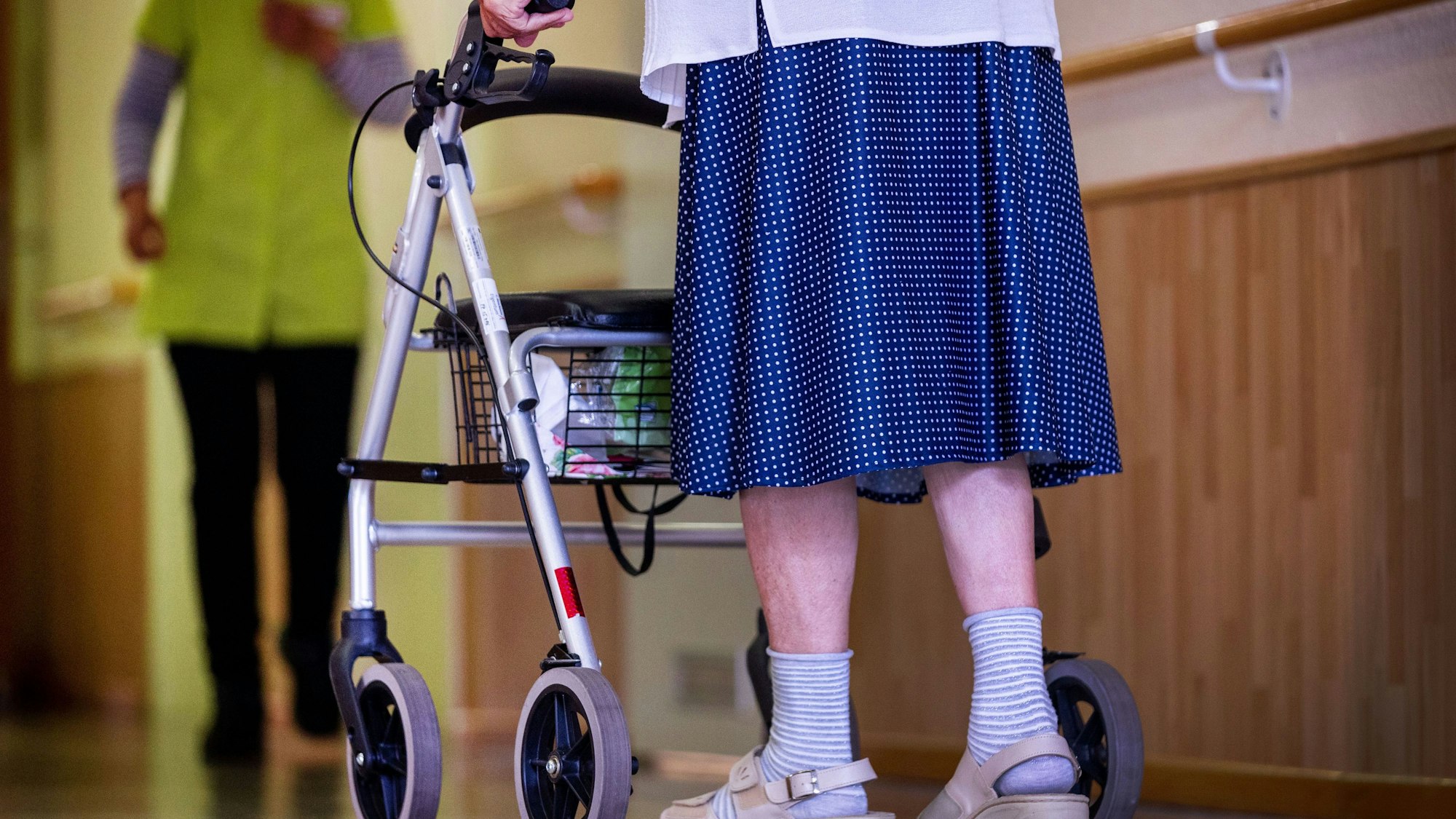 Eine Seniorin geht mit ihrem Rollator über den Gang in einer Pflegeeinrichtung.