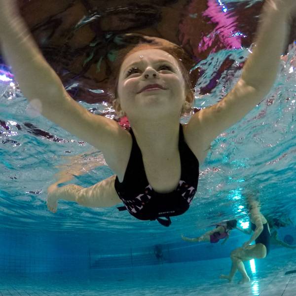 Ein Kind lächelt beim Schwimmen, von Unterwasser fotografiert.