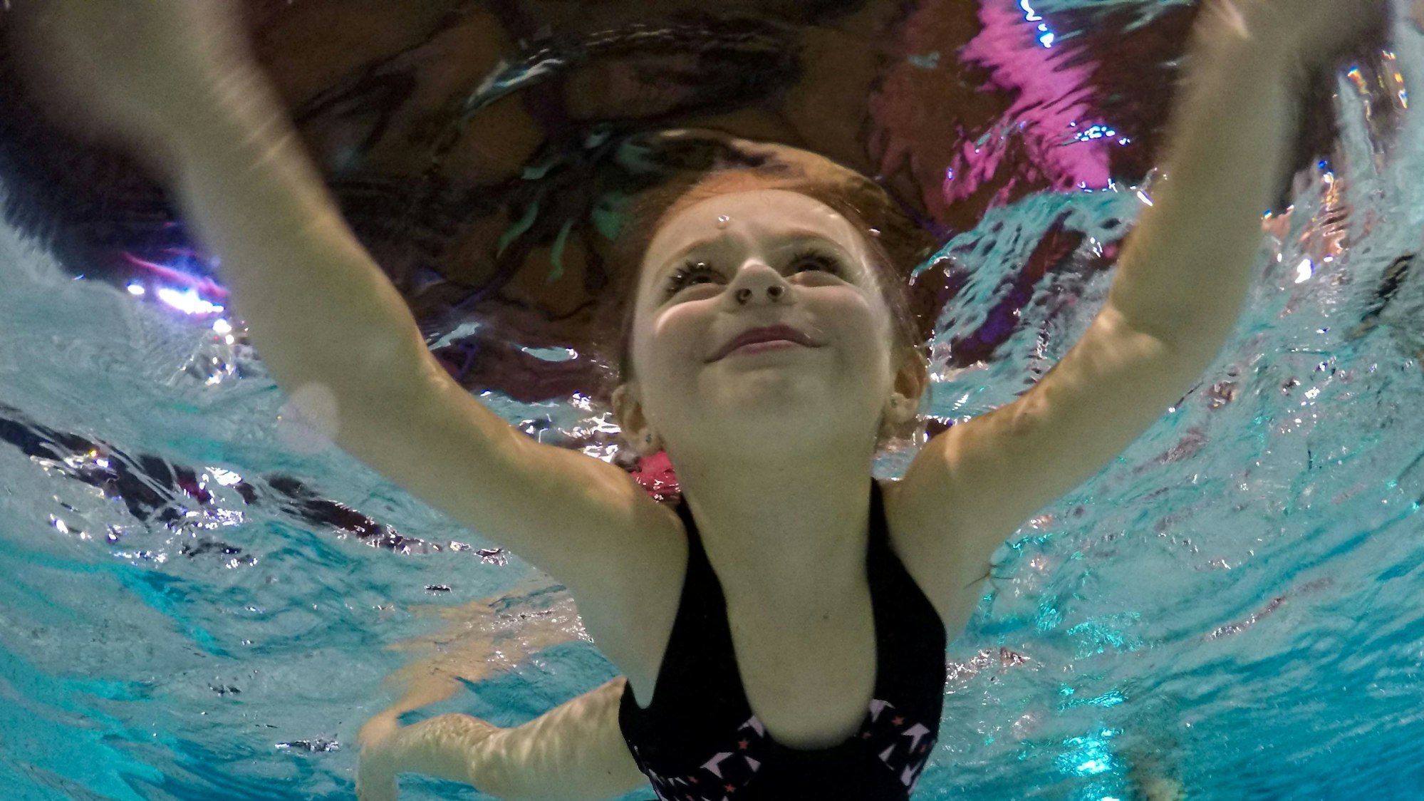 Ein Kind lächelt beim Schwimmen, von Unterwasser fotografiert.