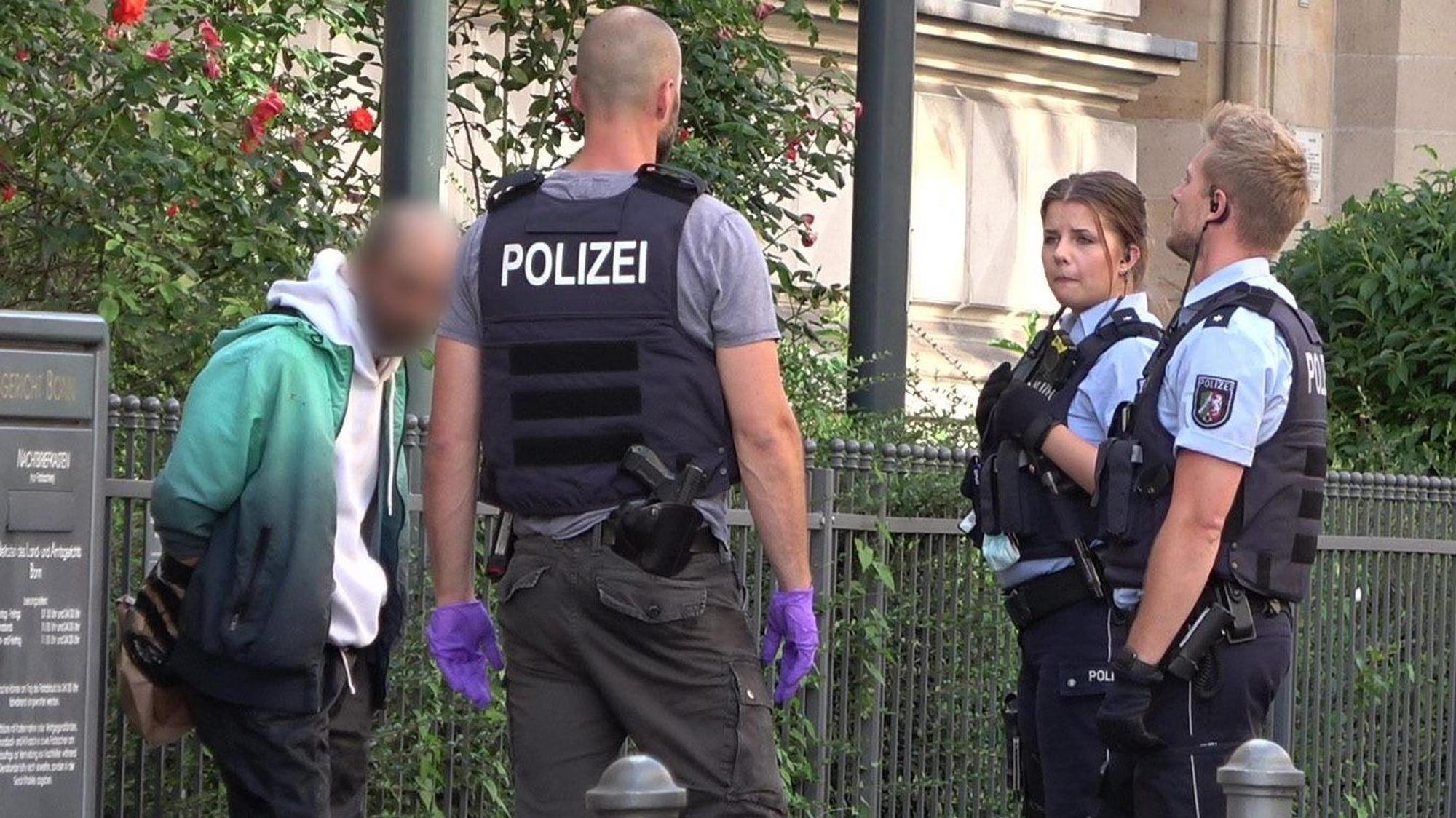 Mehrere Polizisten stehen um einen festgenommenen Mann herum.