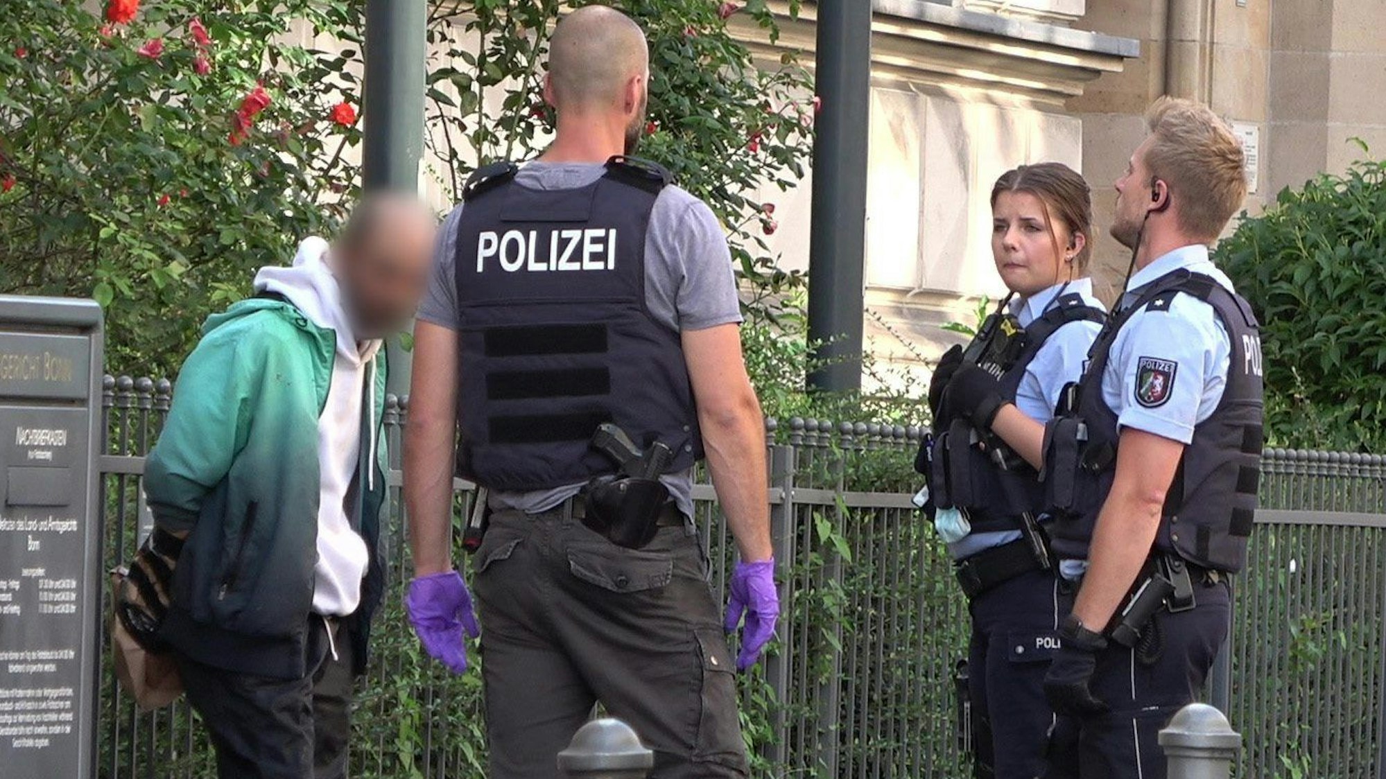 Mehrere Polizisten stehen um einen festgenommenen Mann herum.