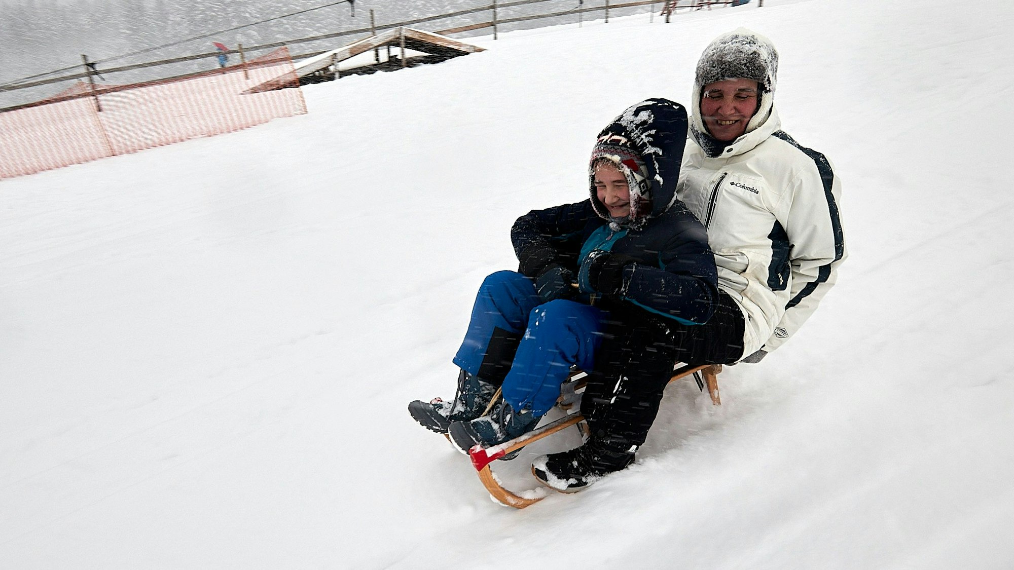 Vater und Sohn sausen auf einem Schlitten den Rodelhang am Weißen Stein hinunter.