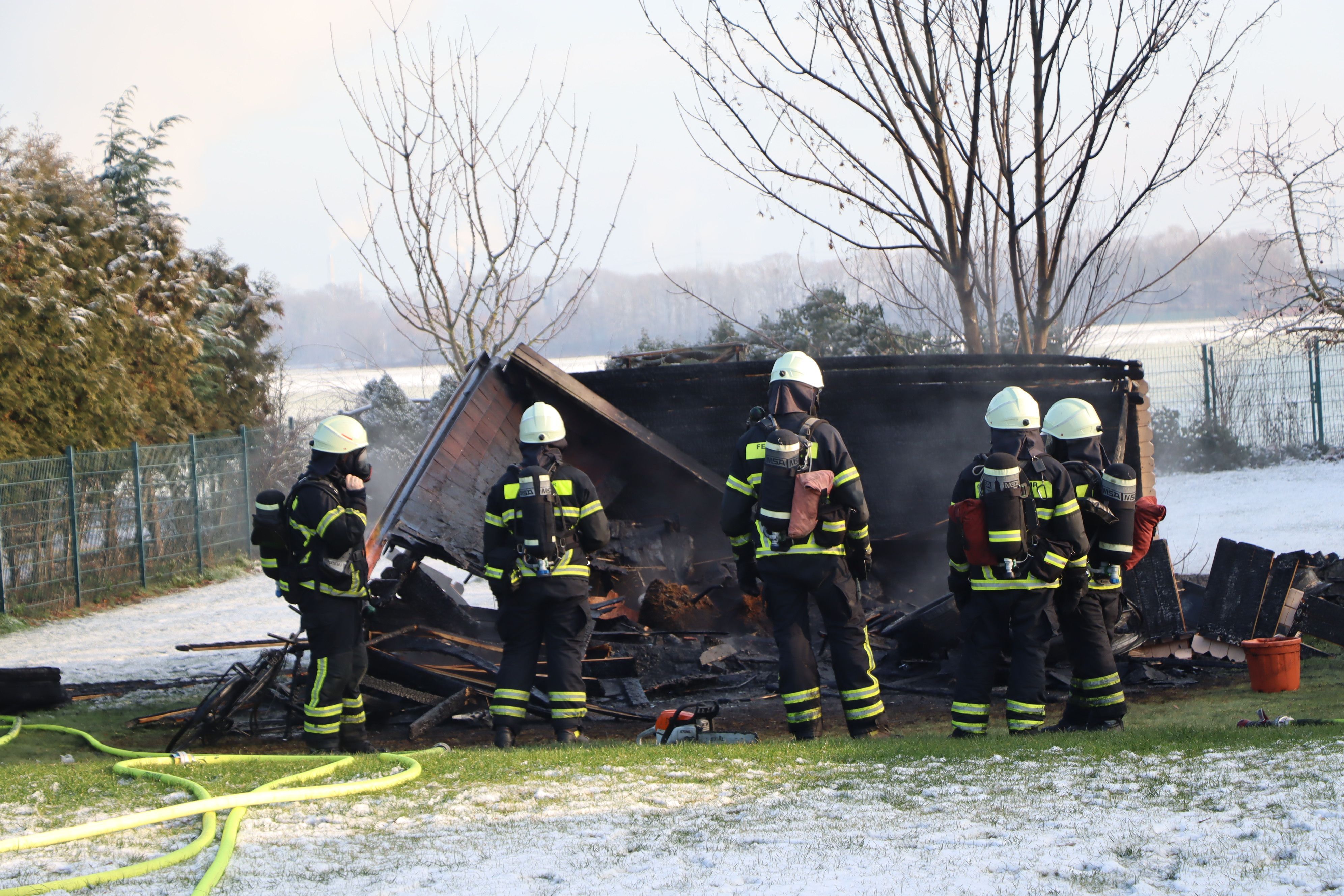 Feuerwehrleute stehen in Ausrüstung vor der eingestürzten Hütte.