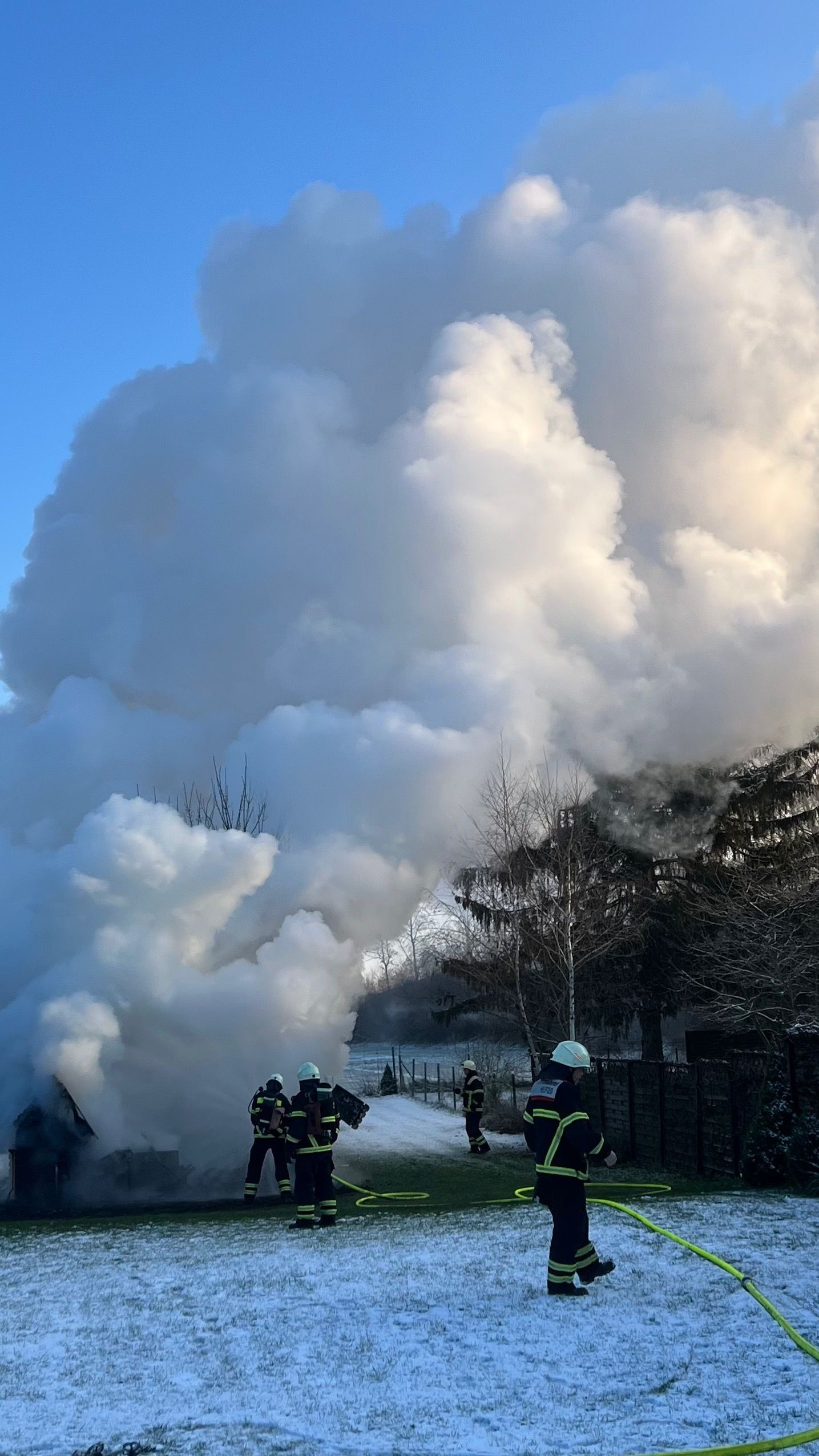 Feuerwehrleute löschen das Haus, eine Wolke aus Rauch und Dampf steigt nach oben.