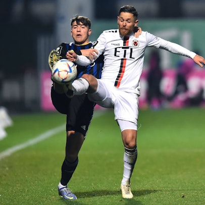 Ein Fußballspieler hält seinen Gegner im Zweikampf am Arm und an der Schulter fest.