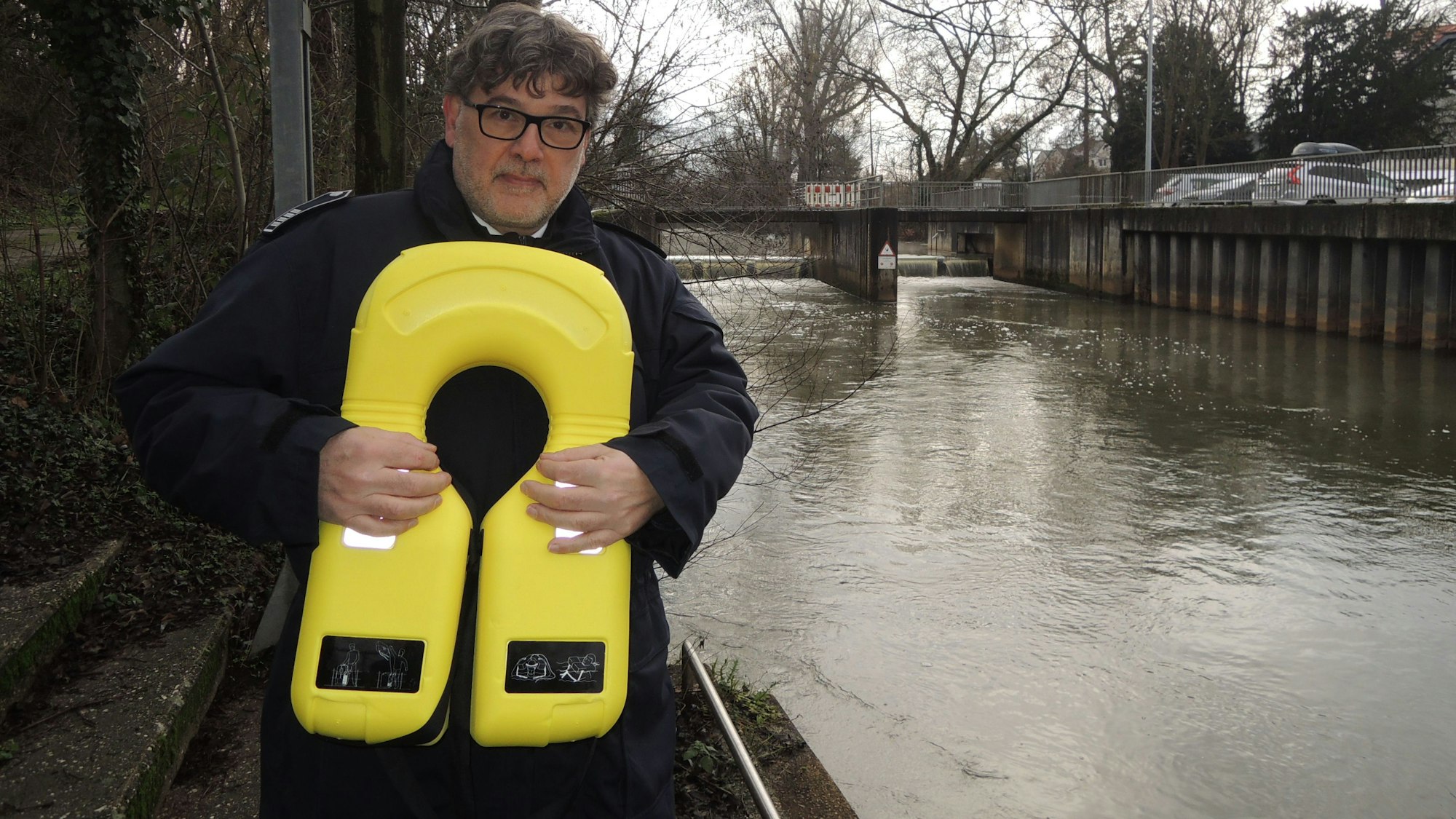 Der Bedburger Feuerwehrchef Guido Garbe mit einem neuen gelben Rettungsgeräte für Ertrinkende. Im Hintergrund ist das Wehr zu sehen.