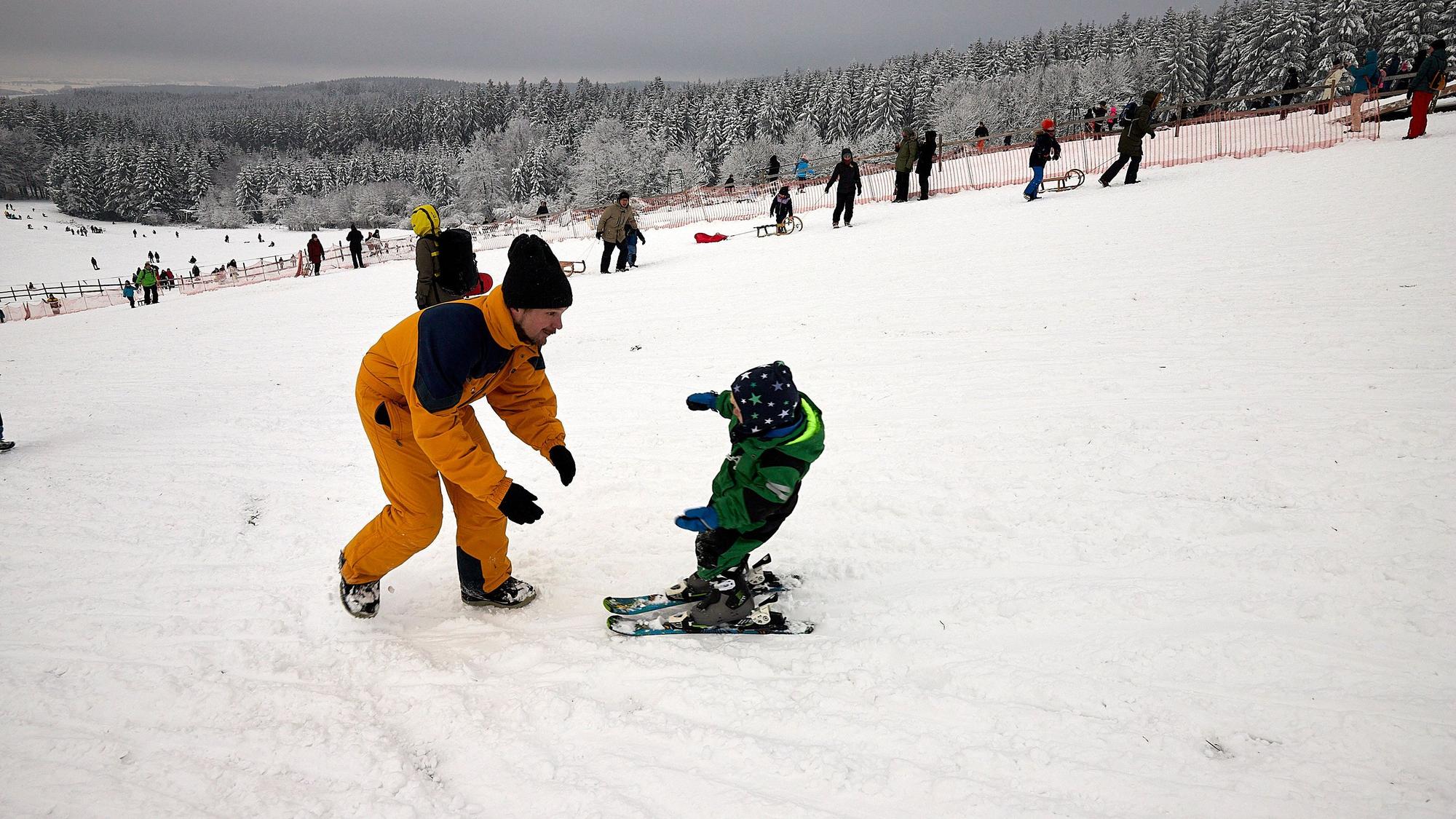 Ein Vater übt mit seinem Sohn auf einer verschneiten Ski-Piste das Ski fahren
