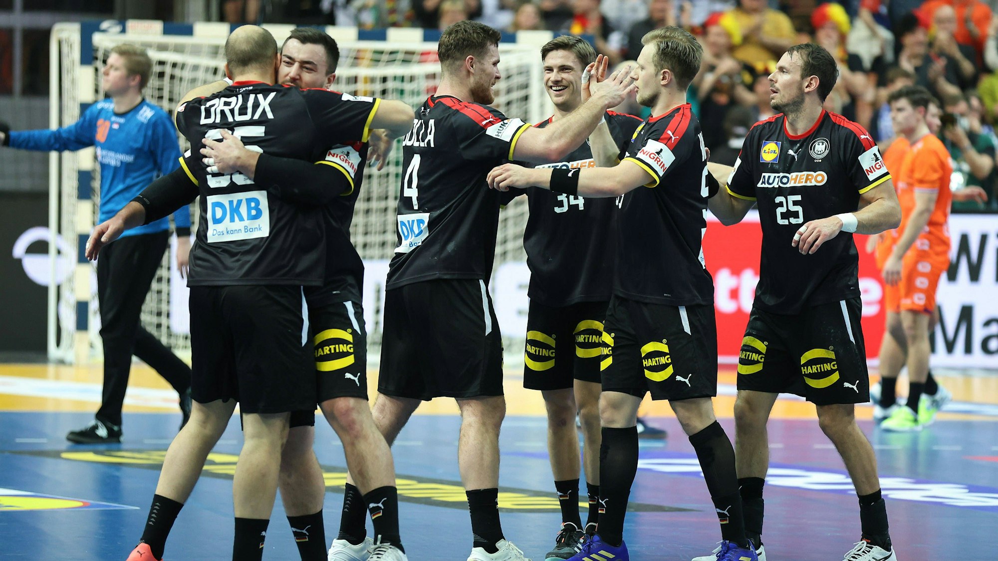 Deutsche Handballspieler, in schwarzen Trikots, freuen sich nach Spielende und liegen sich in den Armen.
