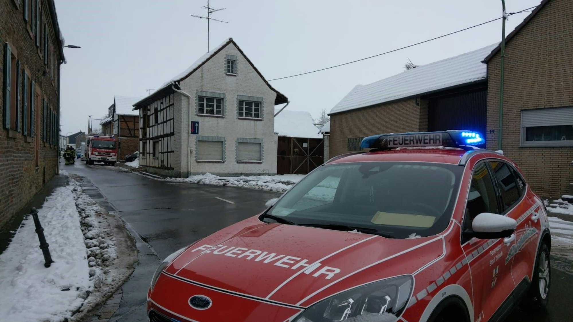 Ein Feuerwehrfahrzeug steht mit eingeschaltetem Blaulicht auf einer Straße.
