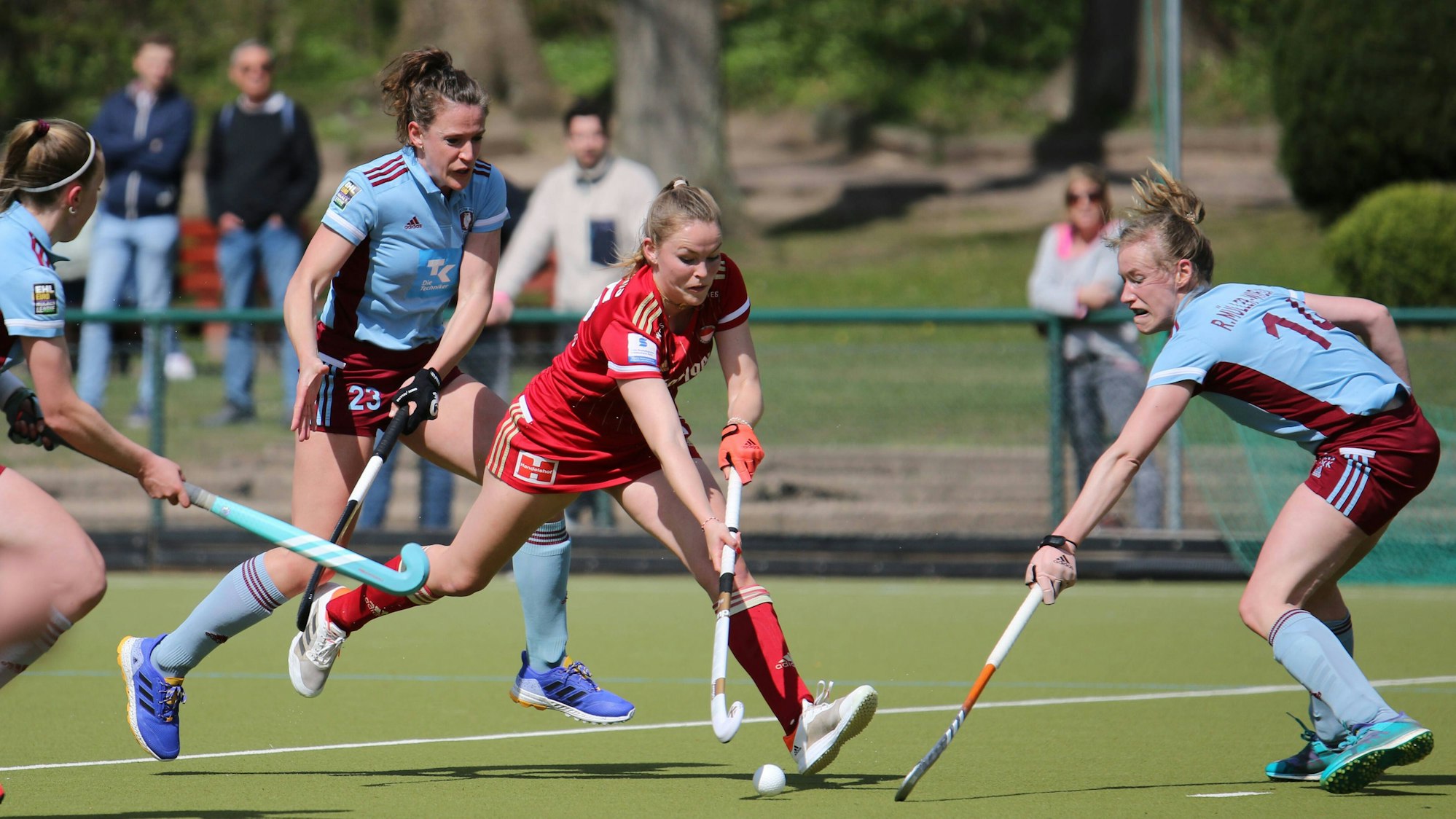 Eine Hockeyspielerin läuft mit dem Ball am Schläger zwischen zwei Gegnerinnen hindurch.
