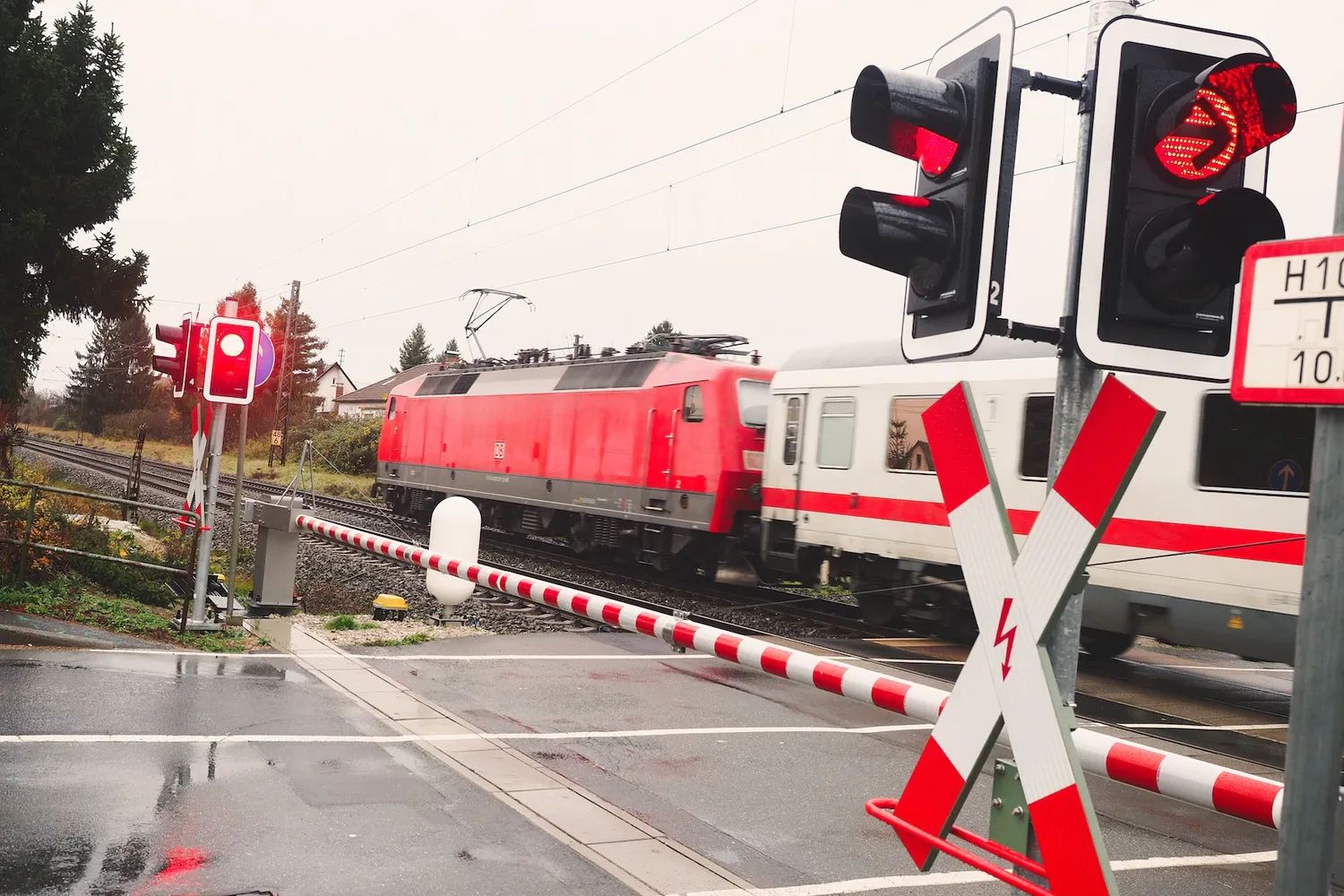 Das Foto zeigt einen Zug, der einen beschrankten Bahnübergang passiert.