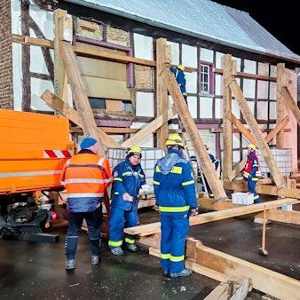Das Foto zeigt die Einsatzstelle mit THW-Leuten, die an einem Fachwerkhaus eine Stützkonstruktion aus Holz errichtet haben.