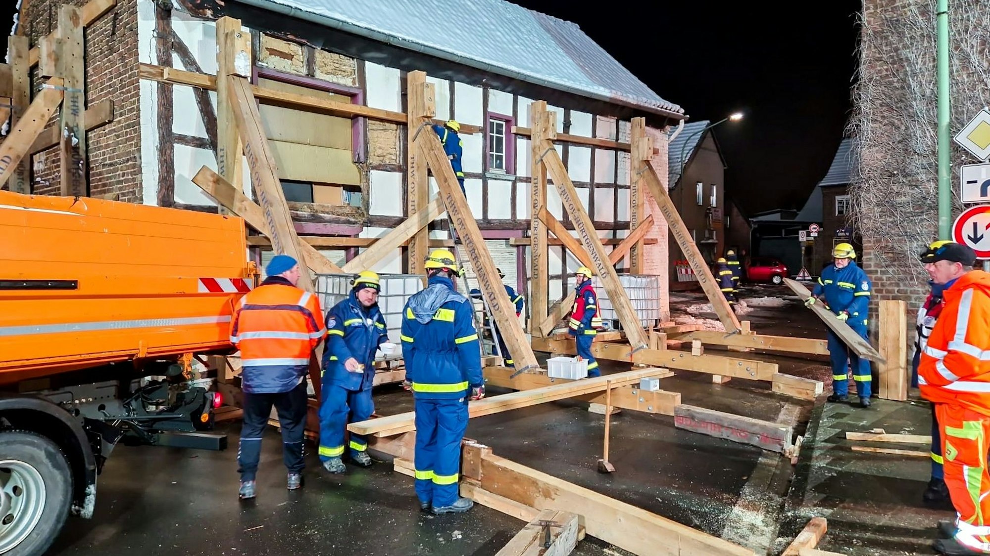 Das Foto zeigt die Einsatzstelle mit THW-Leuten, die an einem Fachwerkhaus eine Stützkonstruktion aus Holz errichtet haben.