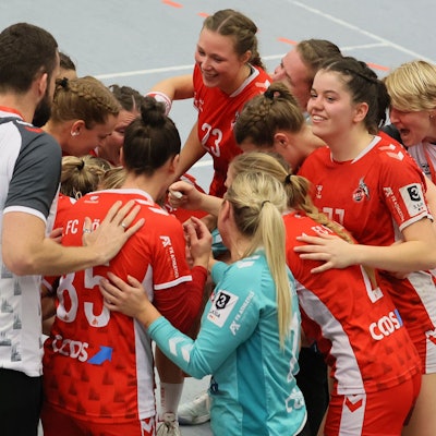 Ein Frauen-Handballteam steht im Kreis zusammen und freut sich über einen Sieg.