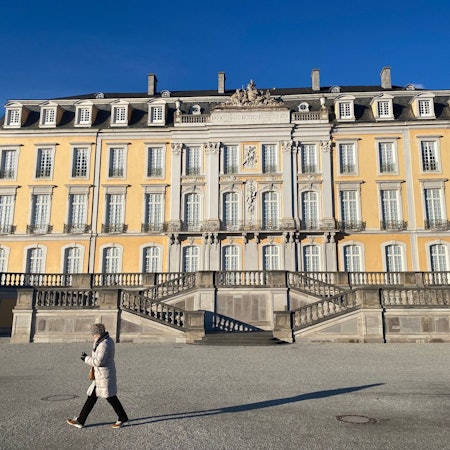 Eine Frau macht einen Spaziergang durch den Brühler Schlosspark. Im Hintergrund ist das Schloss zu sehen.