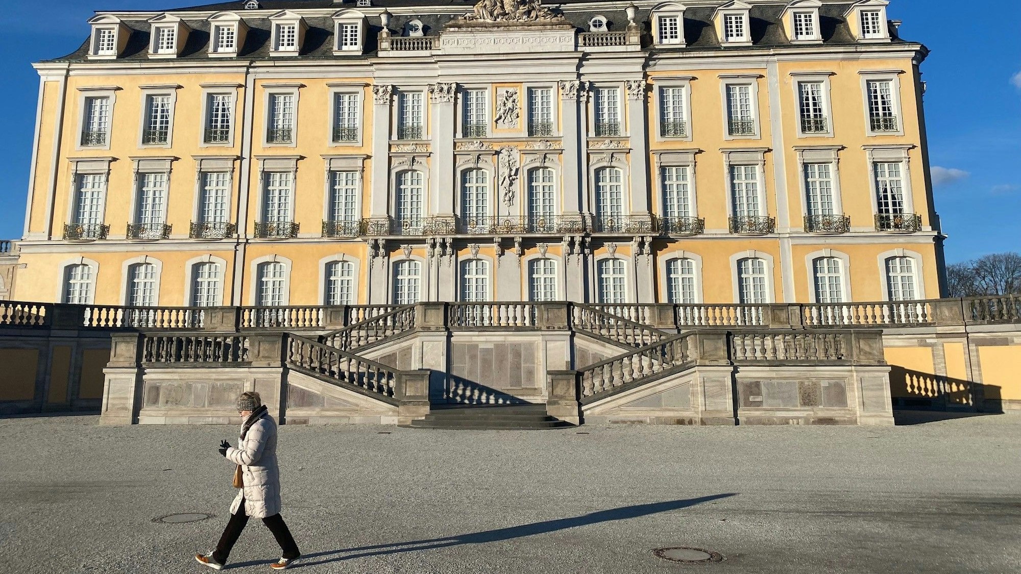 Eine Frau macht einen Spaziergang durch den Brühler Schlosspark. Im Hintergrund ist das Schloss zu sehen.