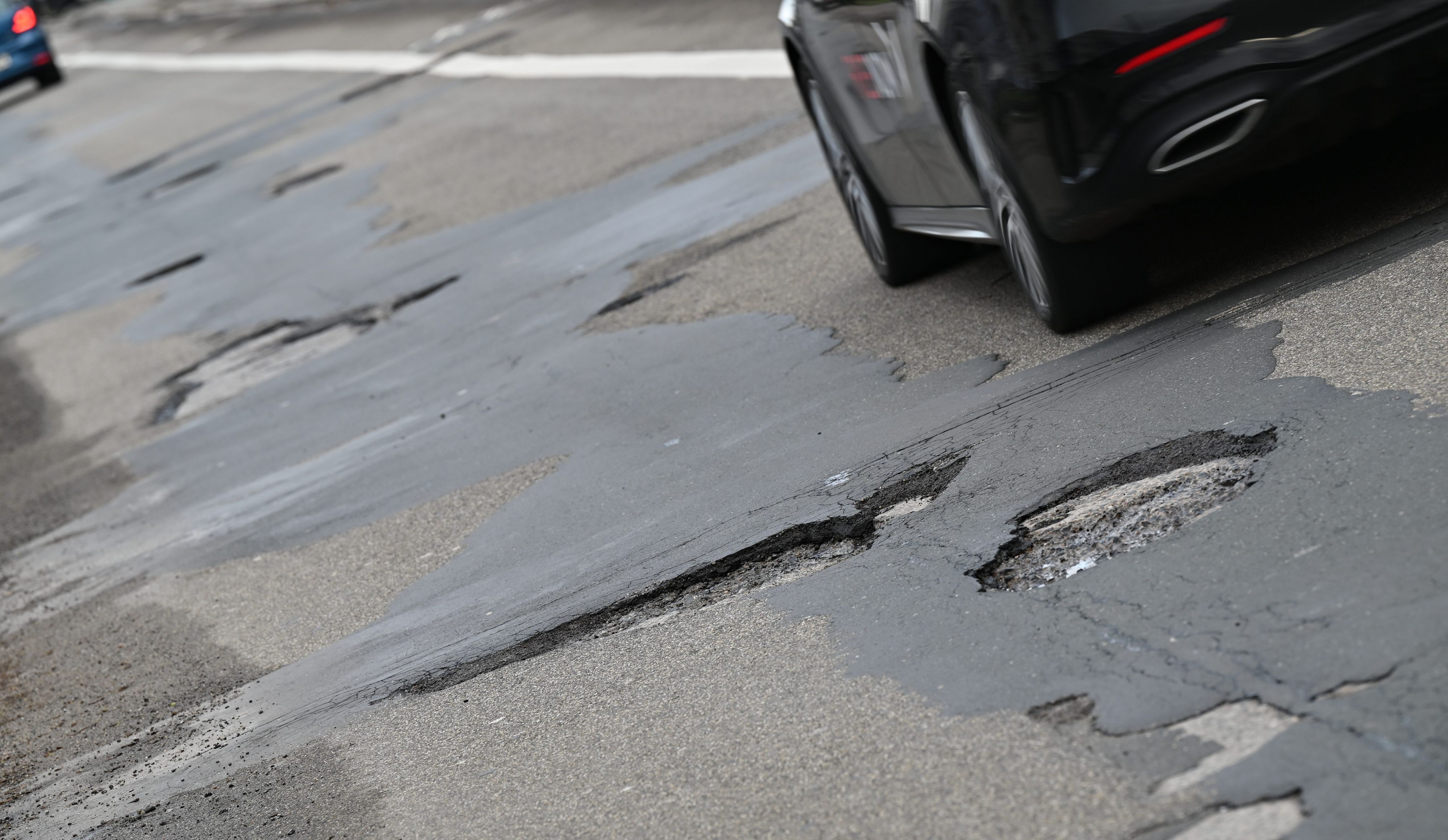 Ein Auto weicht stadteinwärts auf einer Landstraße Schlaglöchern aus.