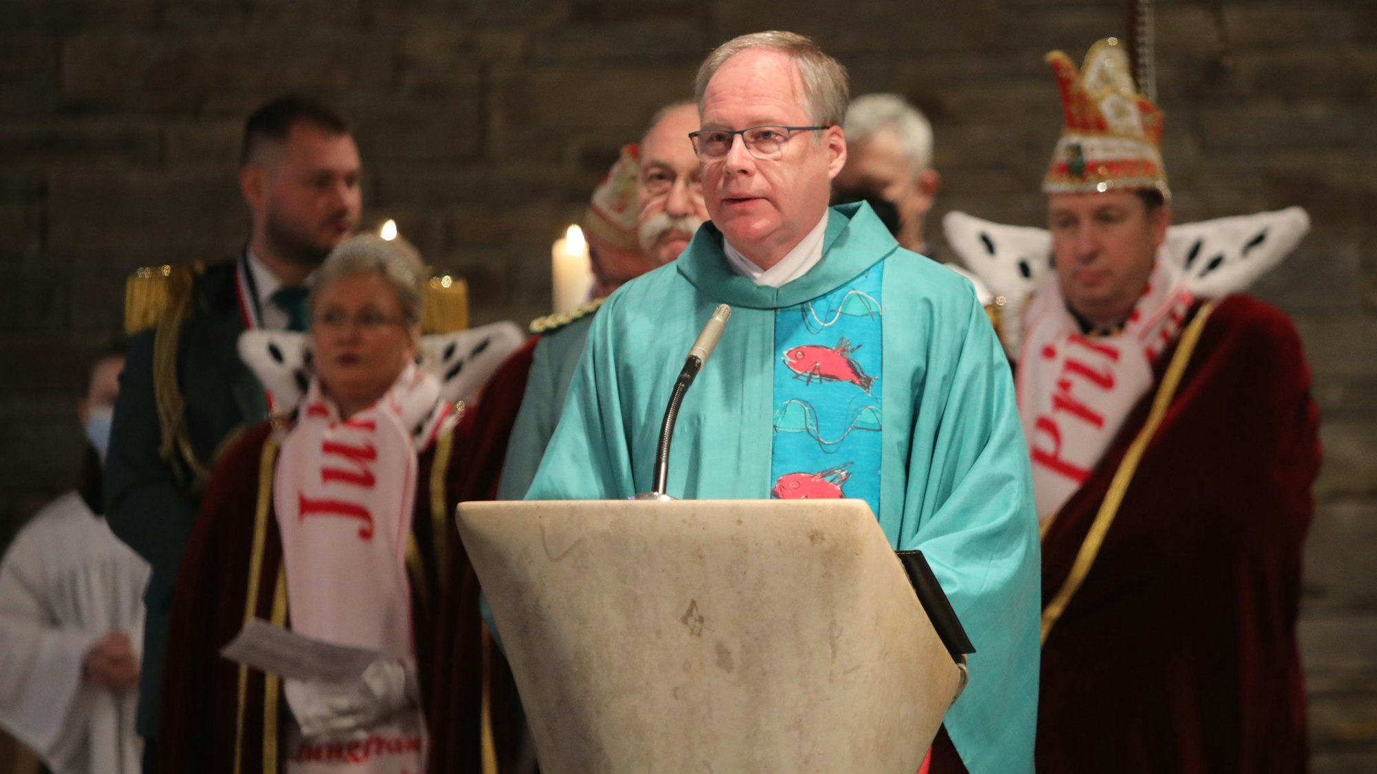 Der katholische Pfarrer Wilhelm Darscheid steht am Ambo der Kirche St. Konrad Hand. Hinter ihm sind Schützen und Karnevalisten zu sehen.