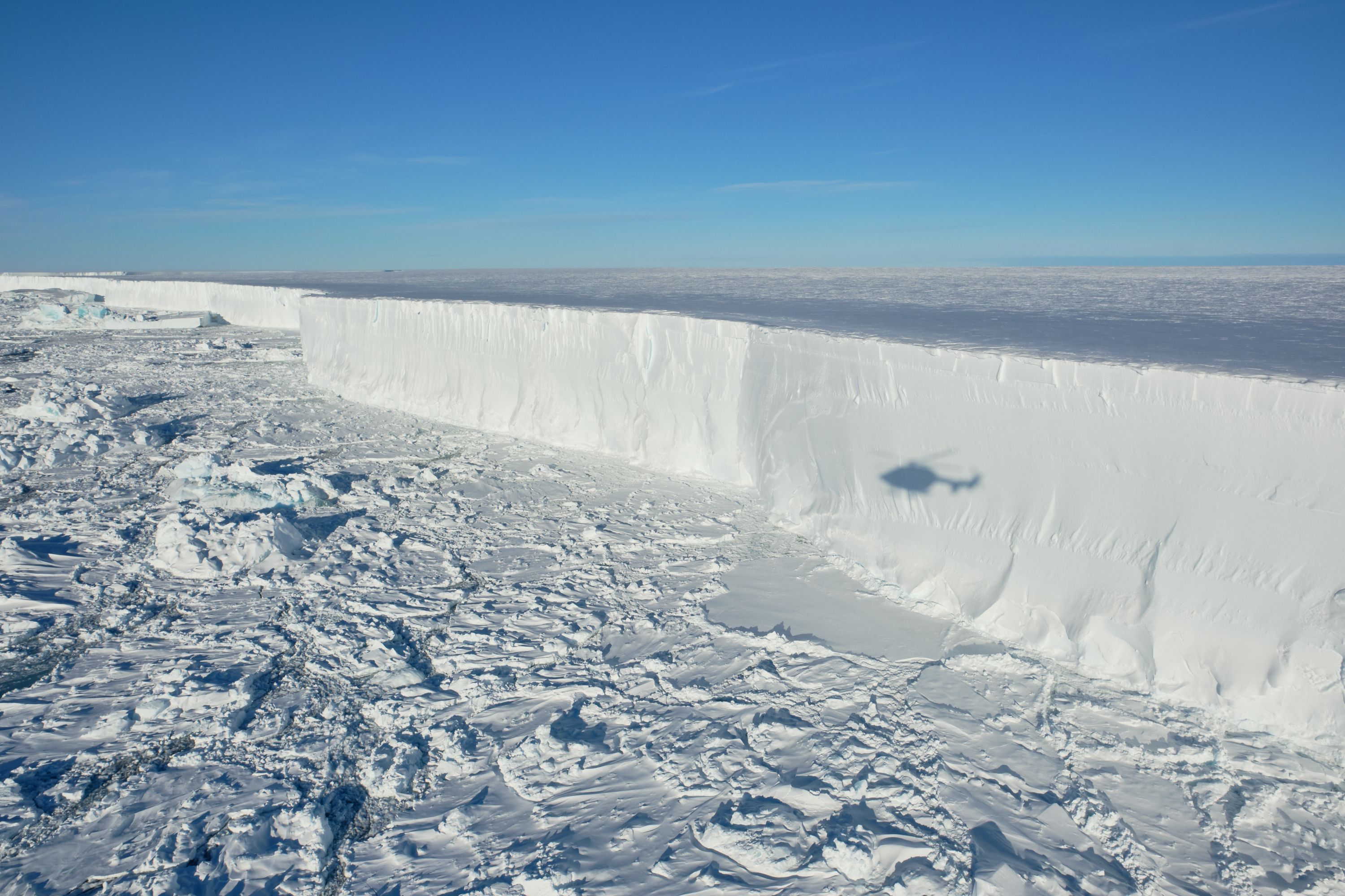 Das Foto zeigt den Eisberg A 74, der sich vom Festland löst, ein Helikopter fliegt darüber.
