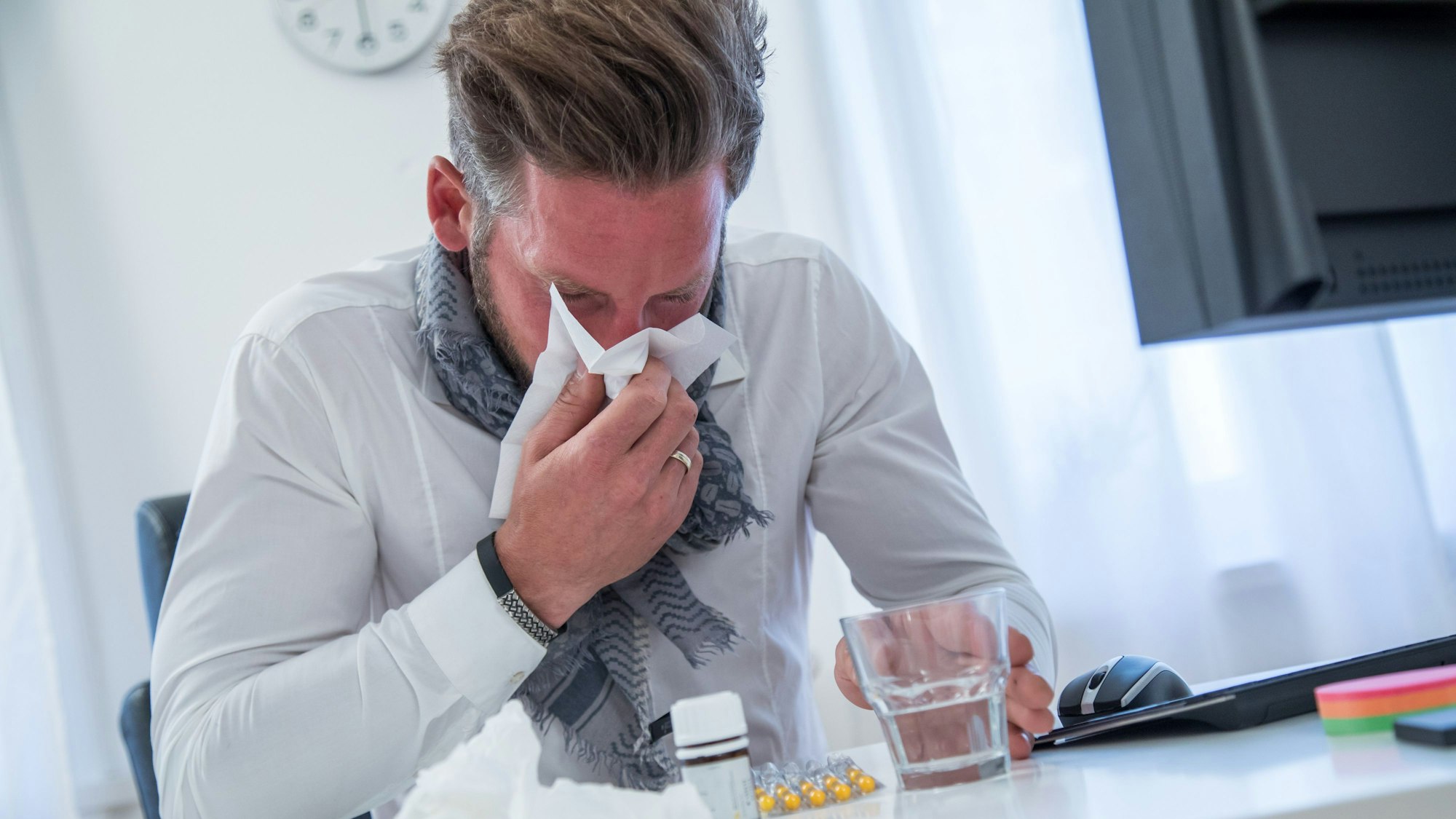 Ein Mann putzt sich am Schreibtisch die Nase.