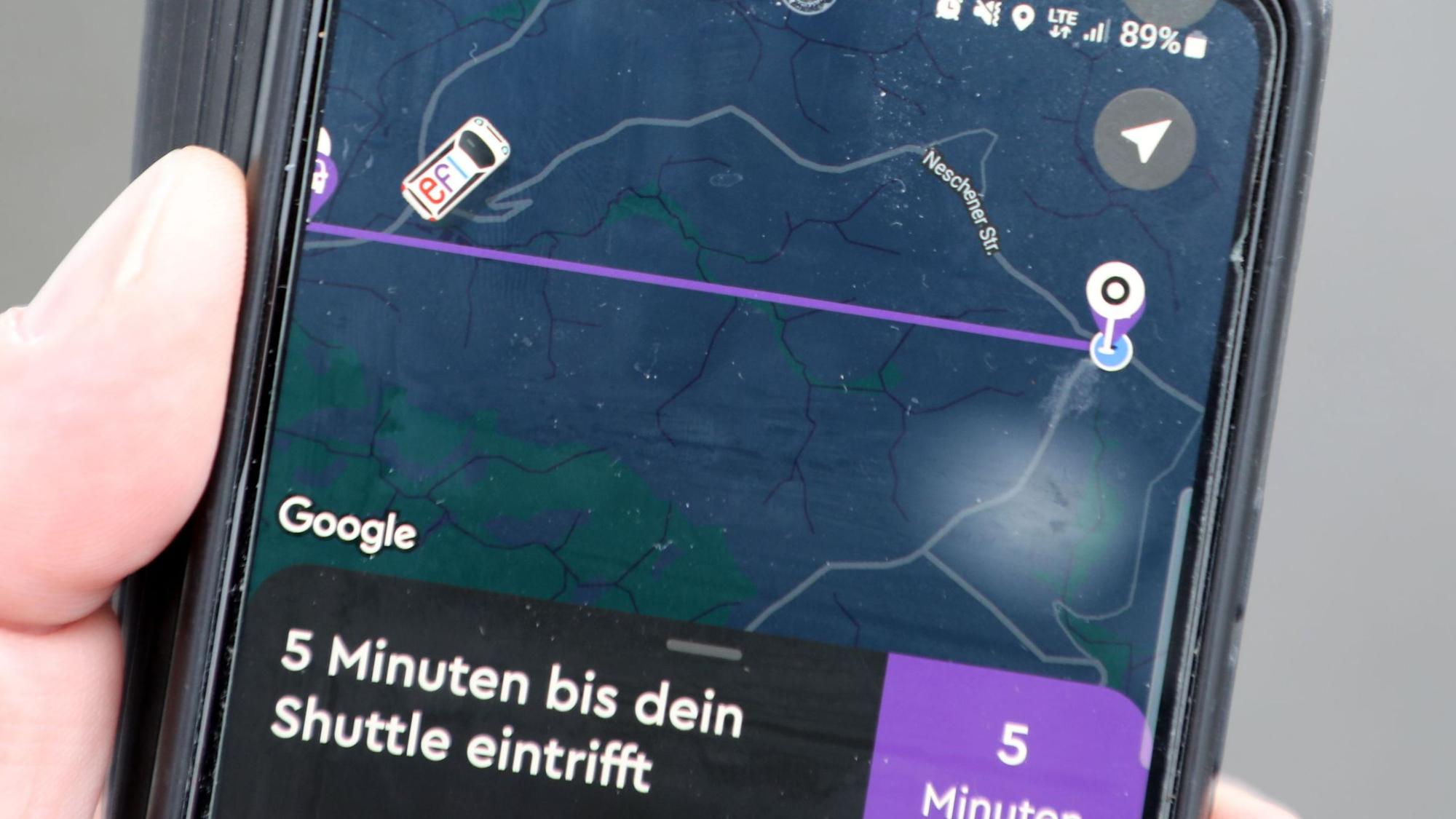 Ein kleines Auto auf dem Bildschirm der „Efi“-App fährt über eine Straße. Darunter steht geschrieben: 5 Minuten, bis dein Shuttle eintrifft.