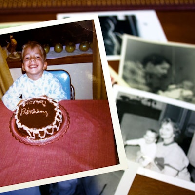 Eine Hand hält ein Foto, auf dem ein Junge vor einem Geburtstagskuchen sitzt.