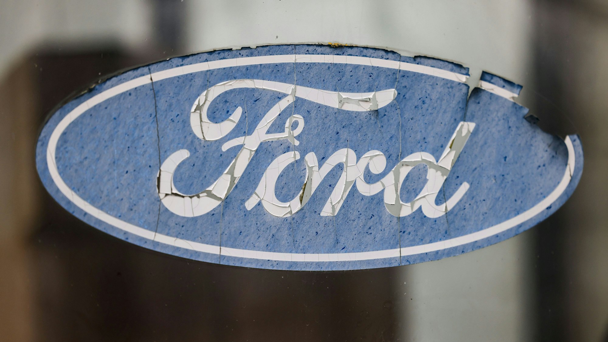 23.01.2023, Nordrhein-Westfalen, Köln: Ein abgeblättertes Logo von Ford hängt an einer Scheibe vor dem Werksgelände. Der Autobauer Ford will an seinem Kölner Standort nach Angaben des Betriebsrats im großen Stil Jobs abbauen.