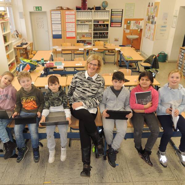 Rektorin Tanja Claßen sitzt mit einigen Schülern und Schülerinnen in einer Klasse auf Tischen.