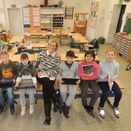 Rektorin Tanja Claßen sitzt mit einigen Schülern und Schülerinnen in einer Klasse auf Tischen.