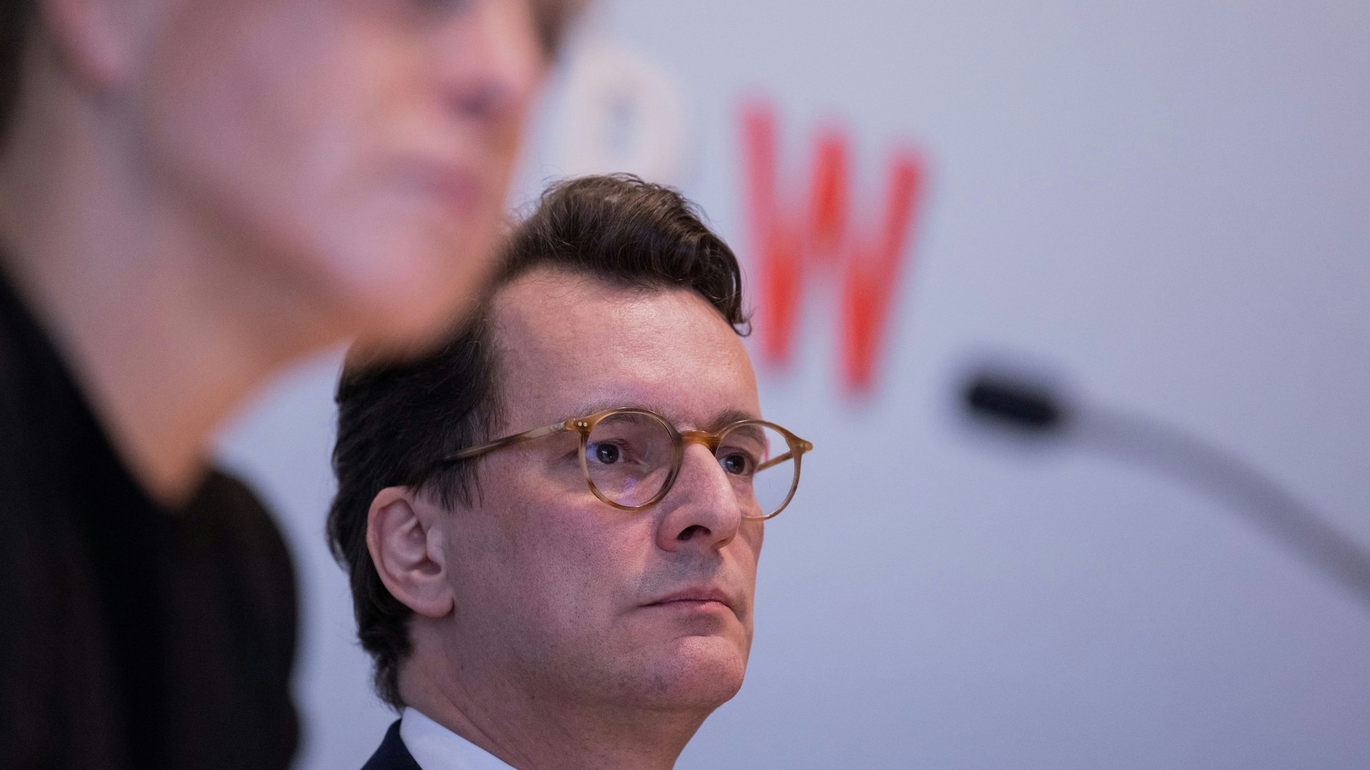 Man sieht Wüsts Gesicht in der Mitte des Bildes, er schaut nach vorne. Hintergrund unscharf, ebenfalls unscharf rechts Neubaur.