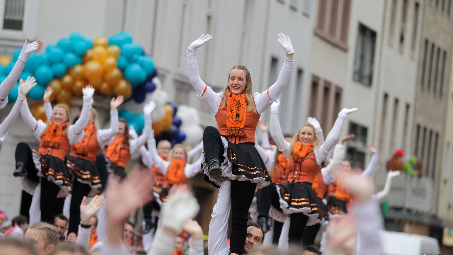 Orange gekleidete Karnevlistinnen und Karnevalisten ziehen beim Rosenmontagszug 2020 durch die Kölner Straßen.