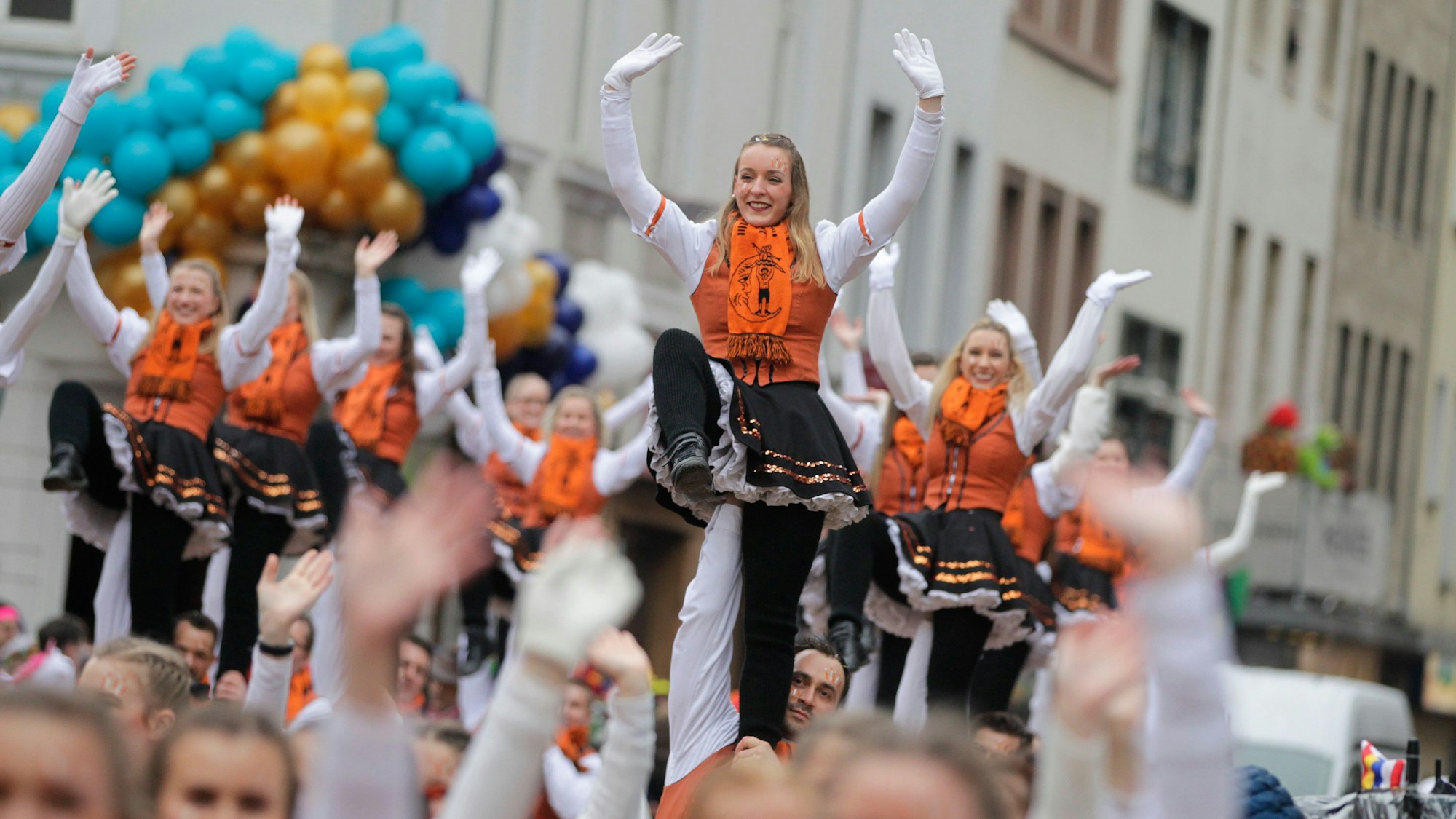 Orange gekleidete Karnevlistinnen und Karnevalisten ziehen beim Rosenmontagszug 2020 durch die Kölner Straßen.