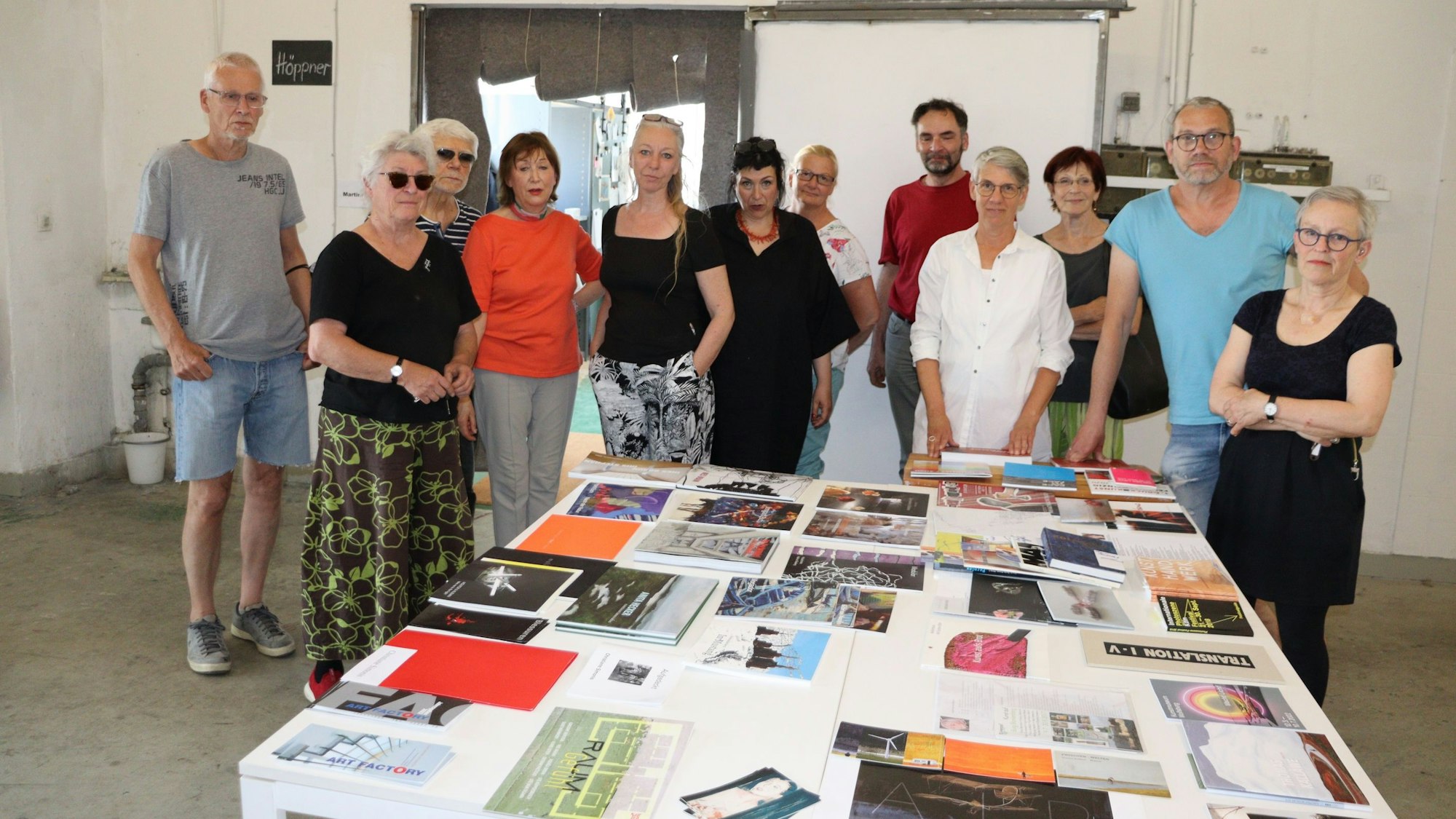 Die Nutzer und Nutzerinnen der Art Factory stehen alle zusammen vor einem großen Tisch.