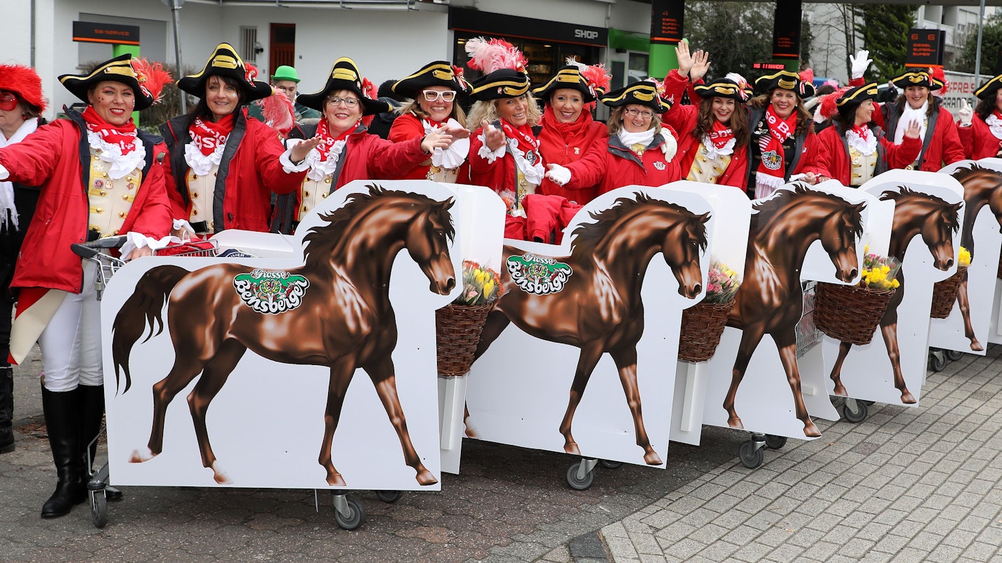 Mehrere Frauen in ihrem Kostüm stehen mit Papppferden auf der Straße.