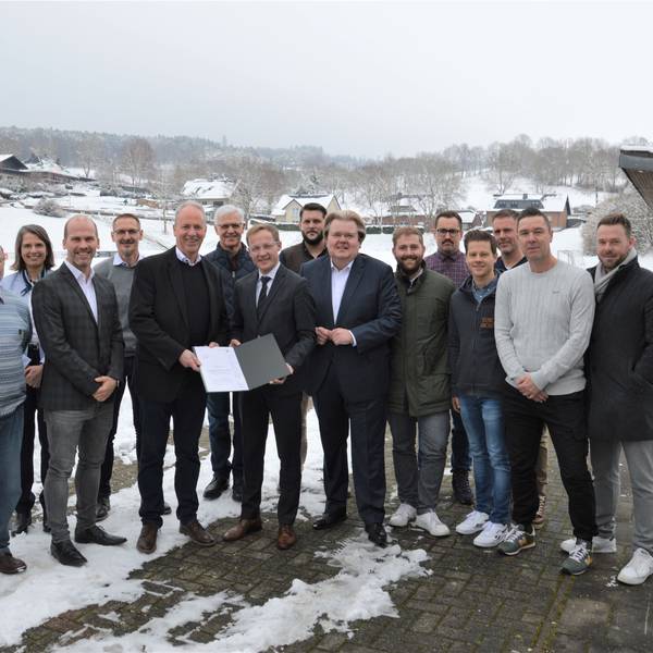 Eine Menschengruppe steht vor einem verschneiten Sportplatz.