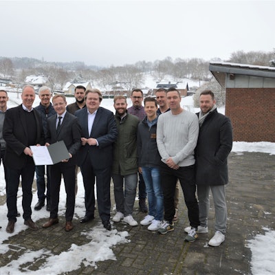 Eine Menschengruppe steht vor einem verschneiten Sportplatz.