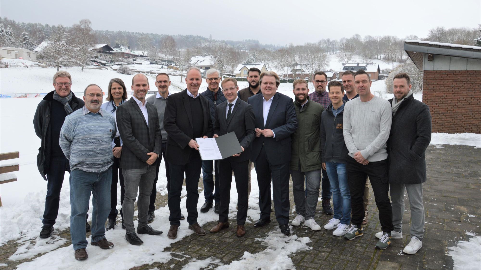 Eine Menschengruppe steht vor einem verschneiten Sportplatz.