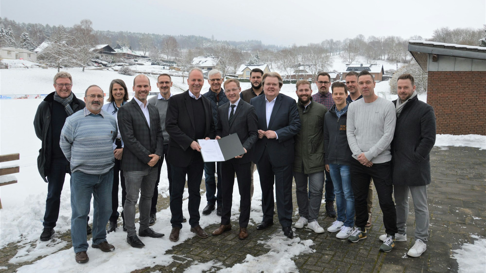 Eine Menschengruppe steht vor einem verschneiten Sportplatz.