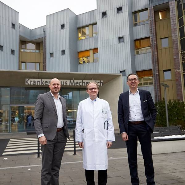Drei Männer, der Mittlere im Arztkittel, stehen vor dem Eingang zum Kreiskrankenhaus Mechernich.