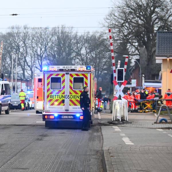Rettungswagen und Polizeiautos stehen vor einem Bahnübergang.