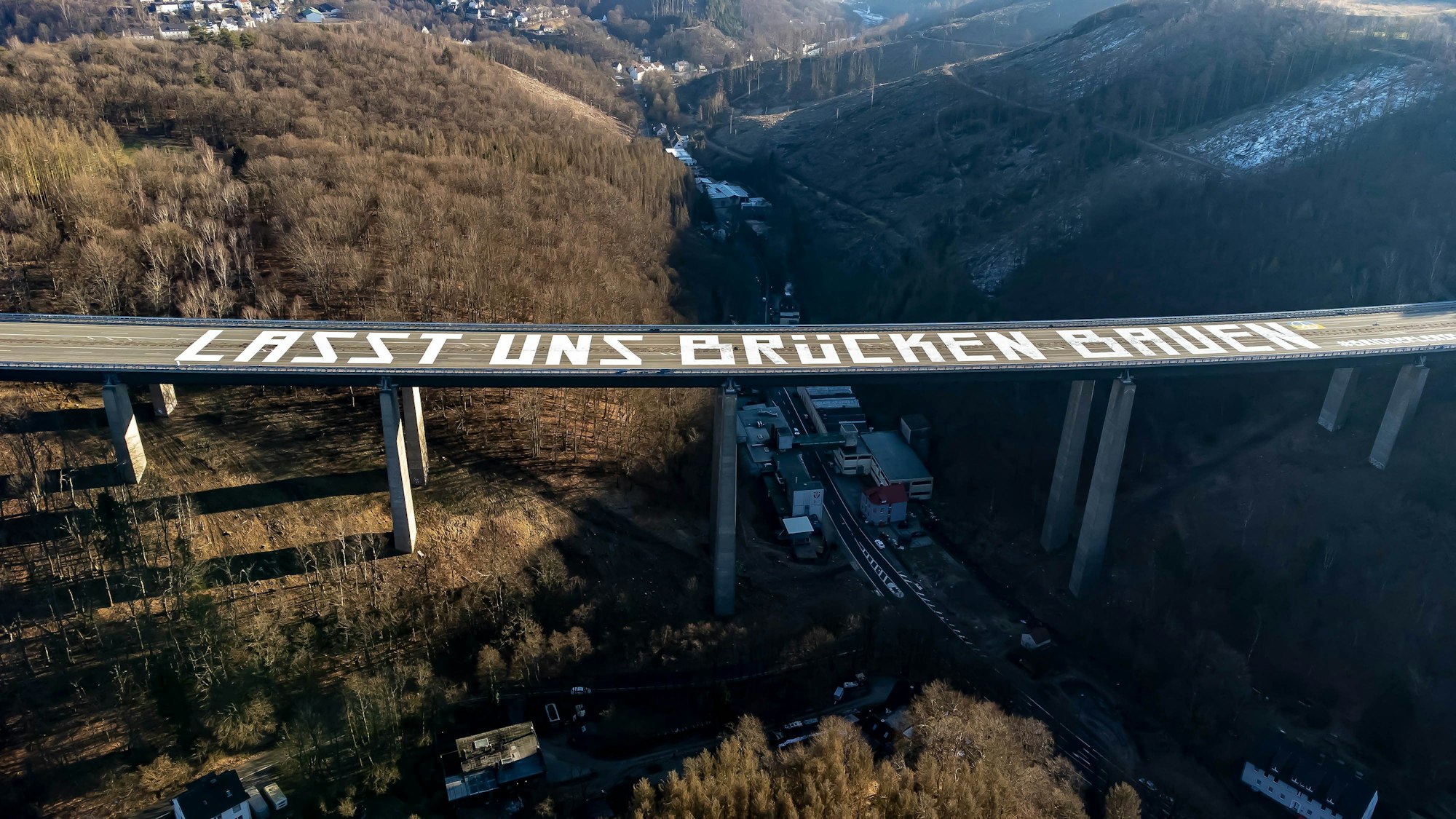 Lüdenscheid: Die Luftaufnahme zeigt die riesige Friedensbotschaft: „Lasst uns Brücken bauen“ auf der gesperrten Rahmedetal-Brücke der Autobahn 45 bei Lüdenscheid (Nordrhein-Westfalen).