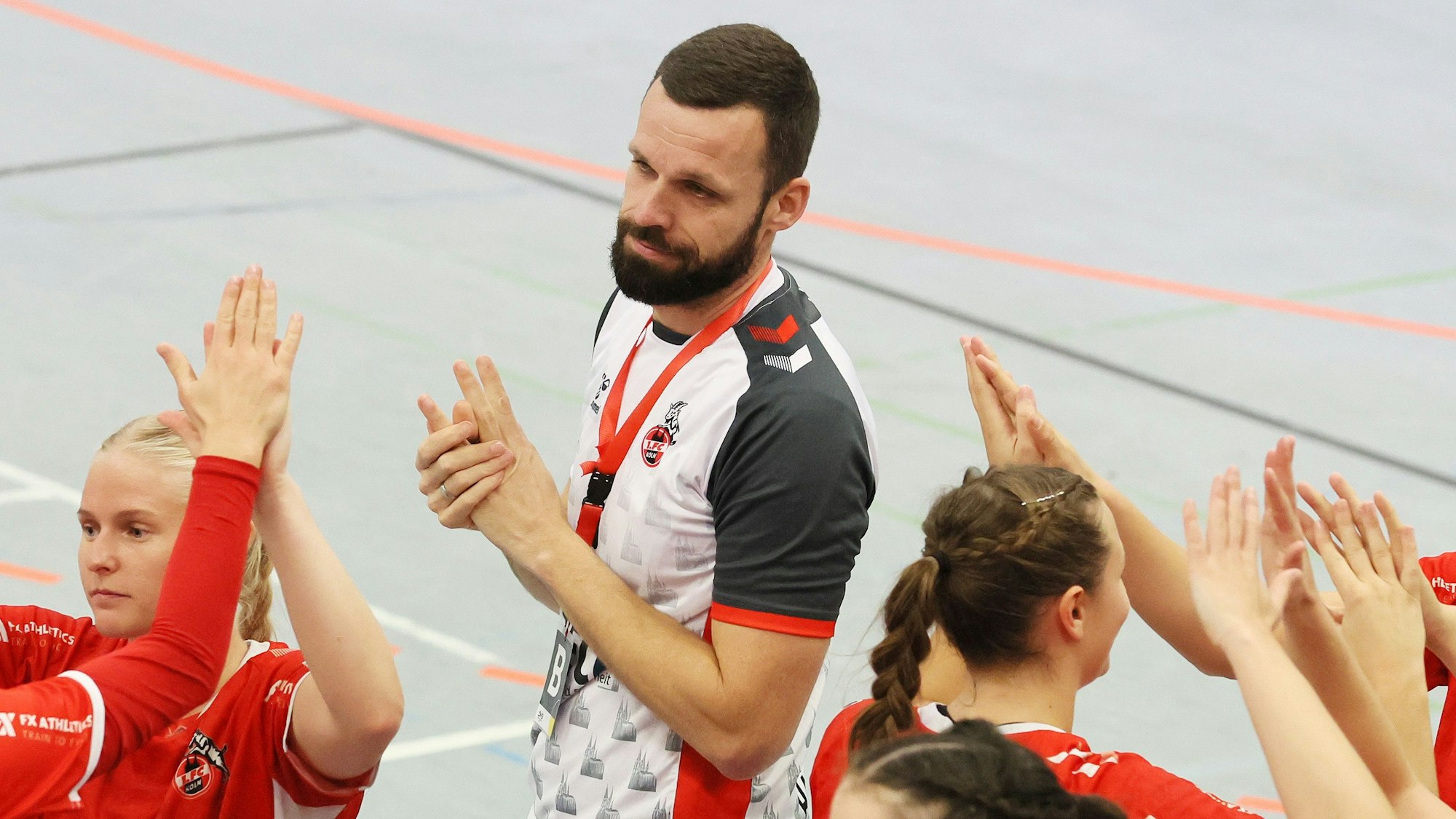 Ein Handballtrainer steht mit einigen seiner Spielerinnen am Spielfeldrand.